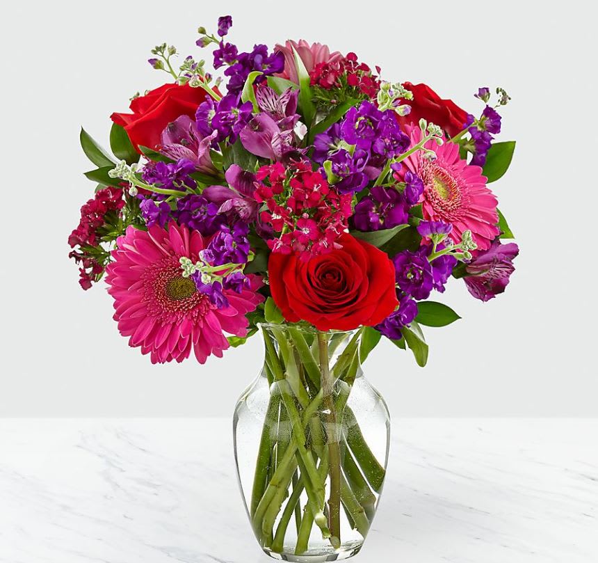 Bouquet of red roses, pink gerbera daisies, and purple flowers in a glass vase