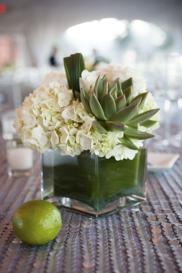 Low white hydrangea and green succulent arrangement in a glass cube vase on a table