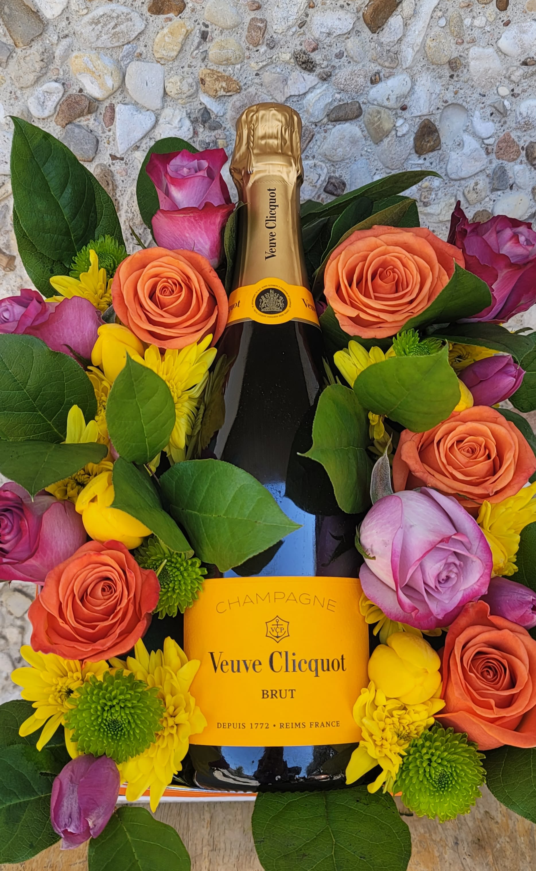 Champagne bottle surrounded by roses and yellow daisies