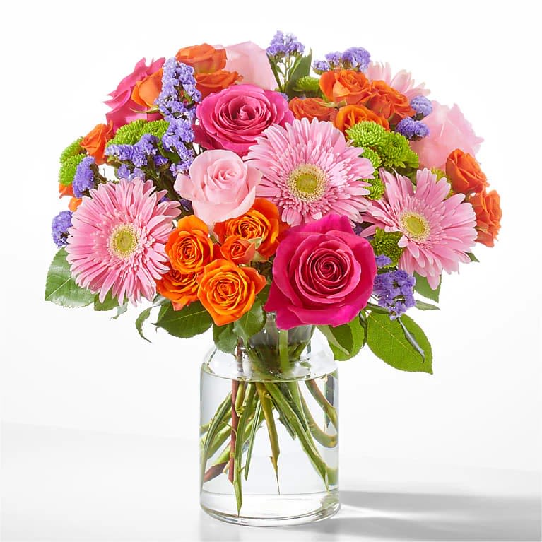 Mixed bouquet of pink, orange, and purple flowers in a clear glass vase