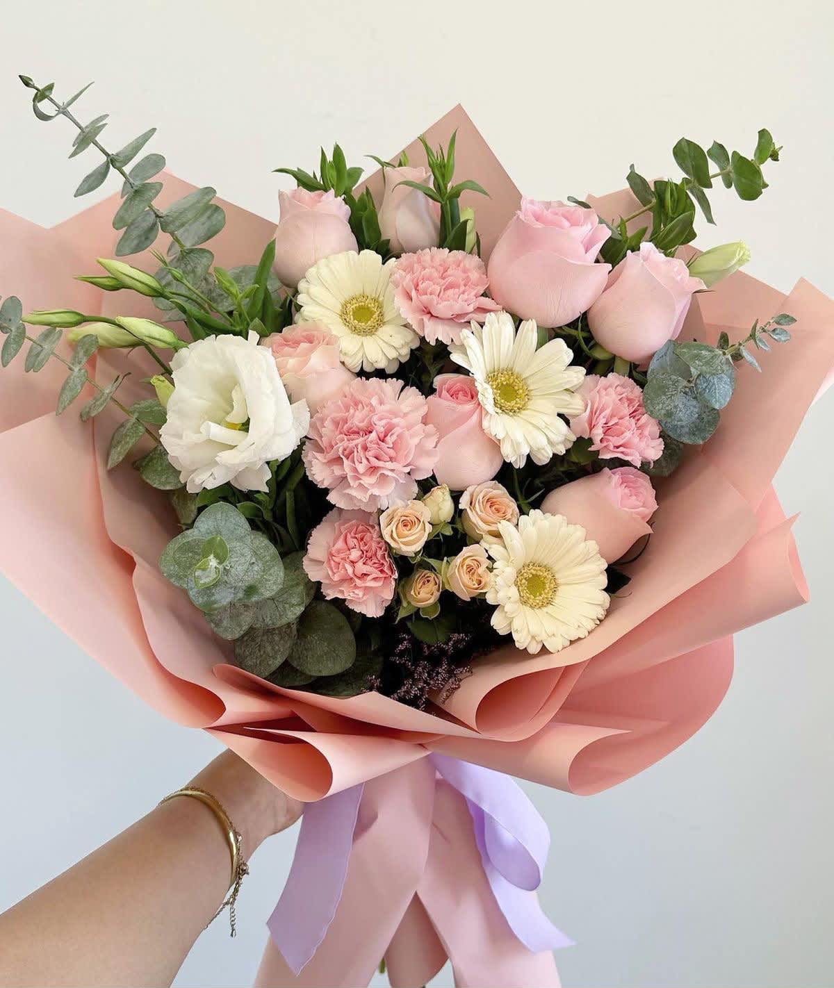 Handheld bouquet of pink roses, white gerbera daisies, and carnations wrapped in pink paper