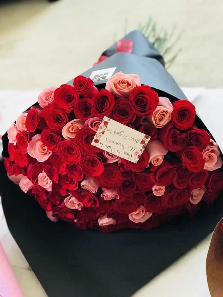 Large bouquet of red and pink roses wrapped in black paper with a small card attached