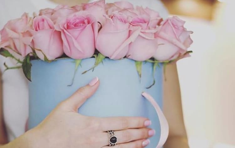 Pink roses arranged in a light blue hatbox with a ribbon handle