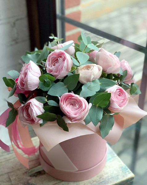 Pink Happiness - Pink ranunculus with eucalyptus and seeded greens in a medium pink box. Ranunculus opens slowly over several days, so it looks fuller at the end of the week than on the day it arrives. No vase needed.