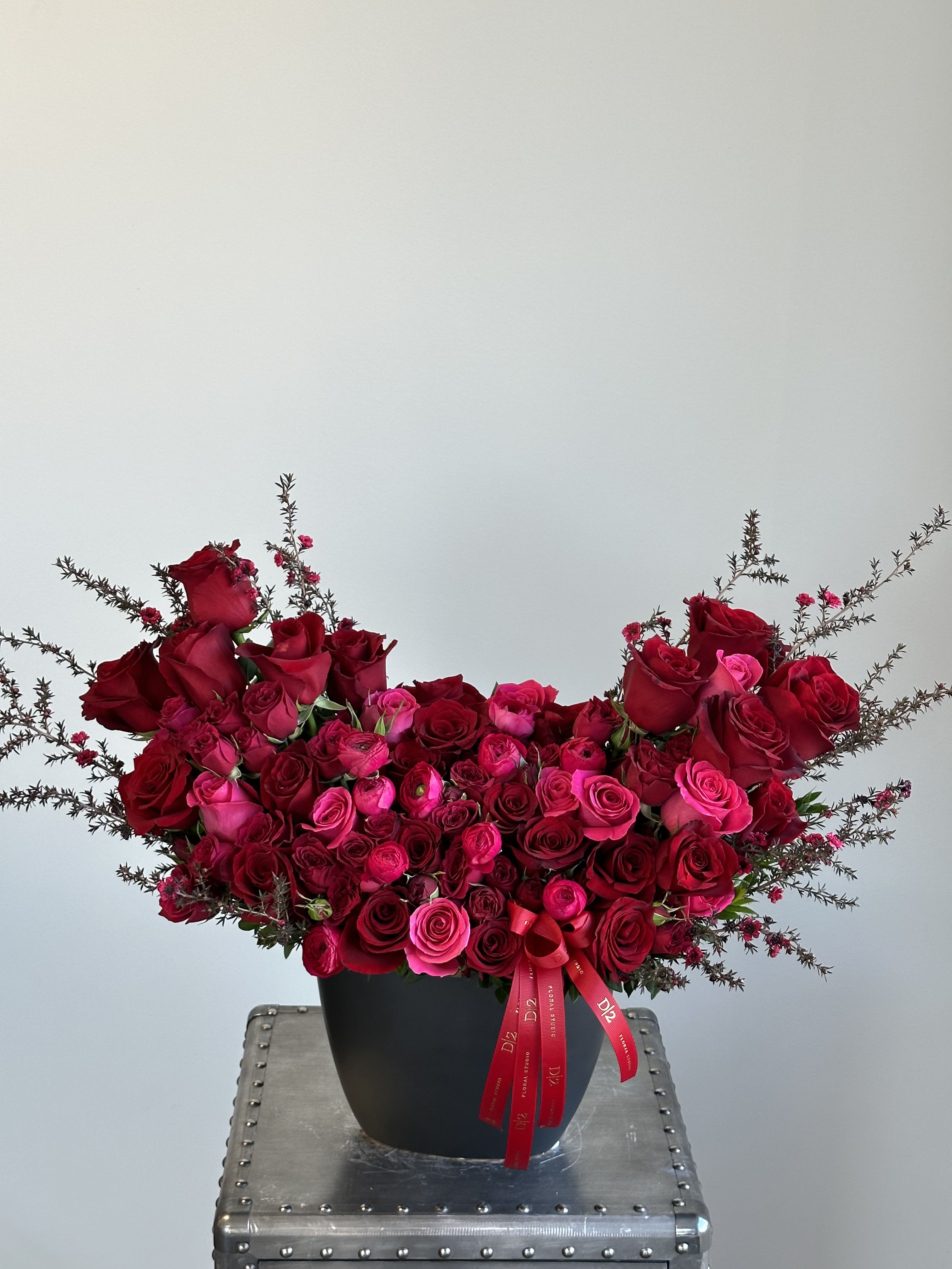 Red and pink rose arrangement in a black vase with ribbon
