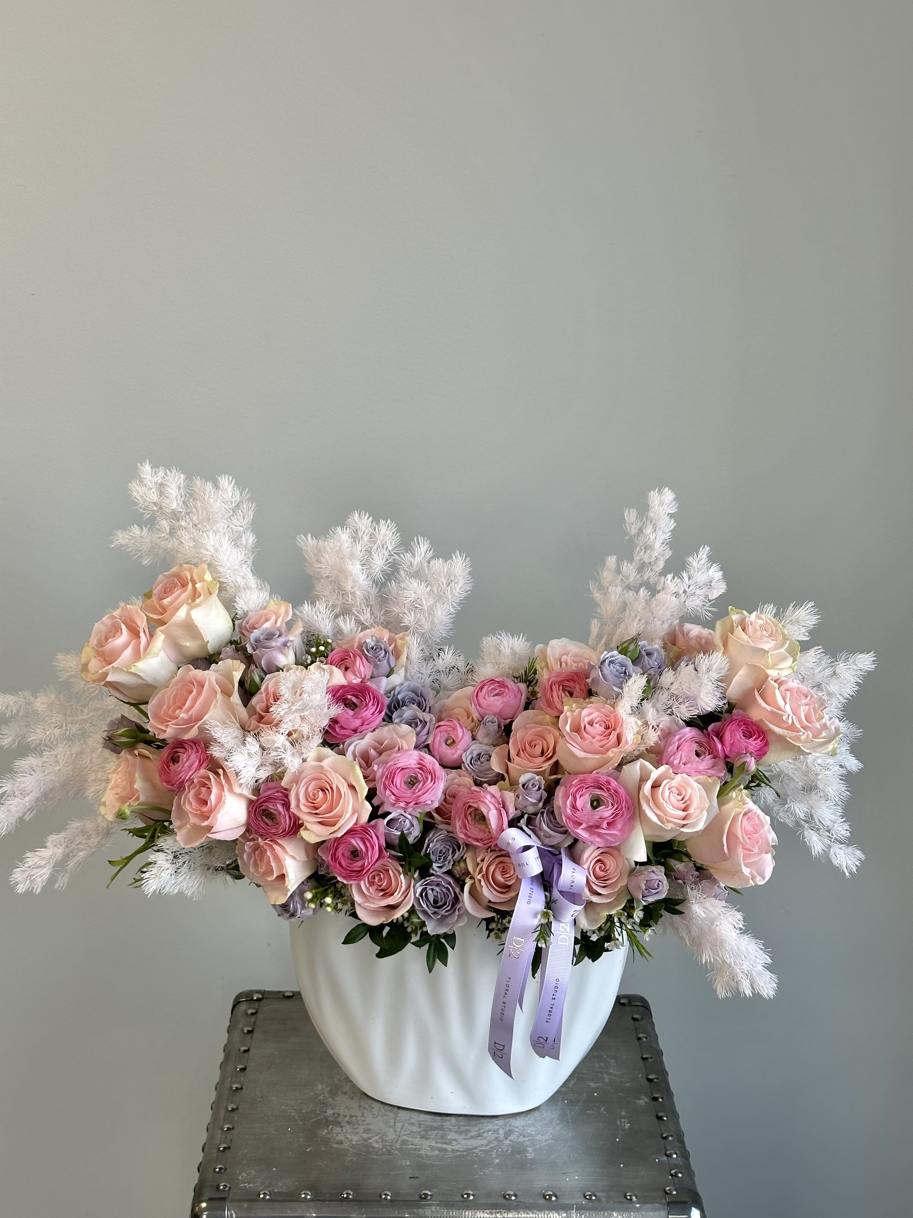 Pink and lavender roses arranged in a white vase with fluffy white accents