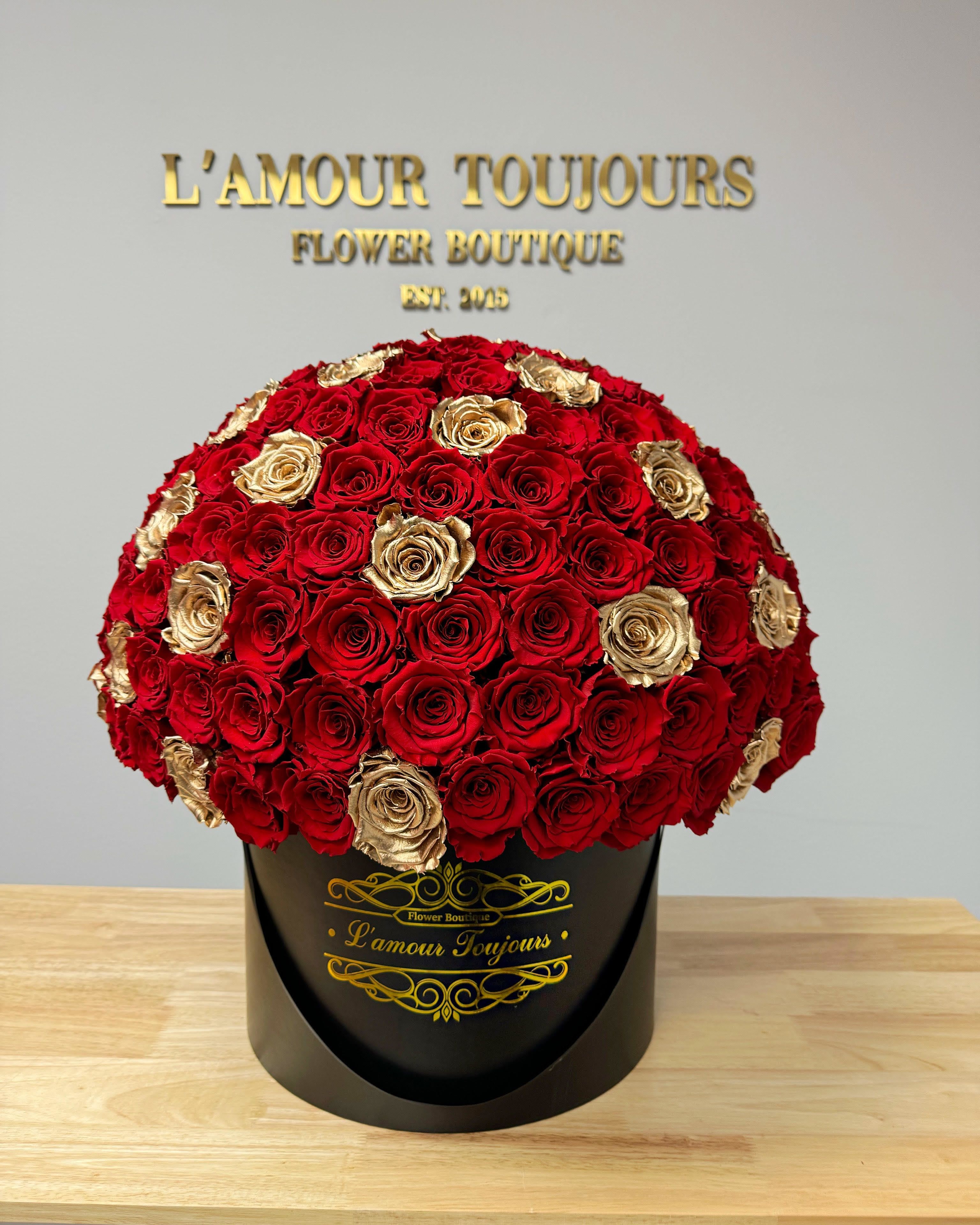 Round bouquet of red and gold roses in a black hatbox