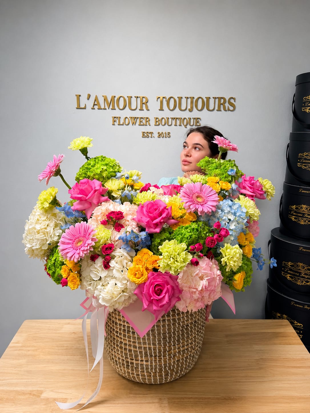 Large mixed flower arrangement in a woven basket with pink ribbon