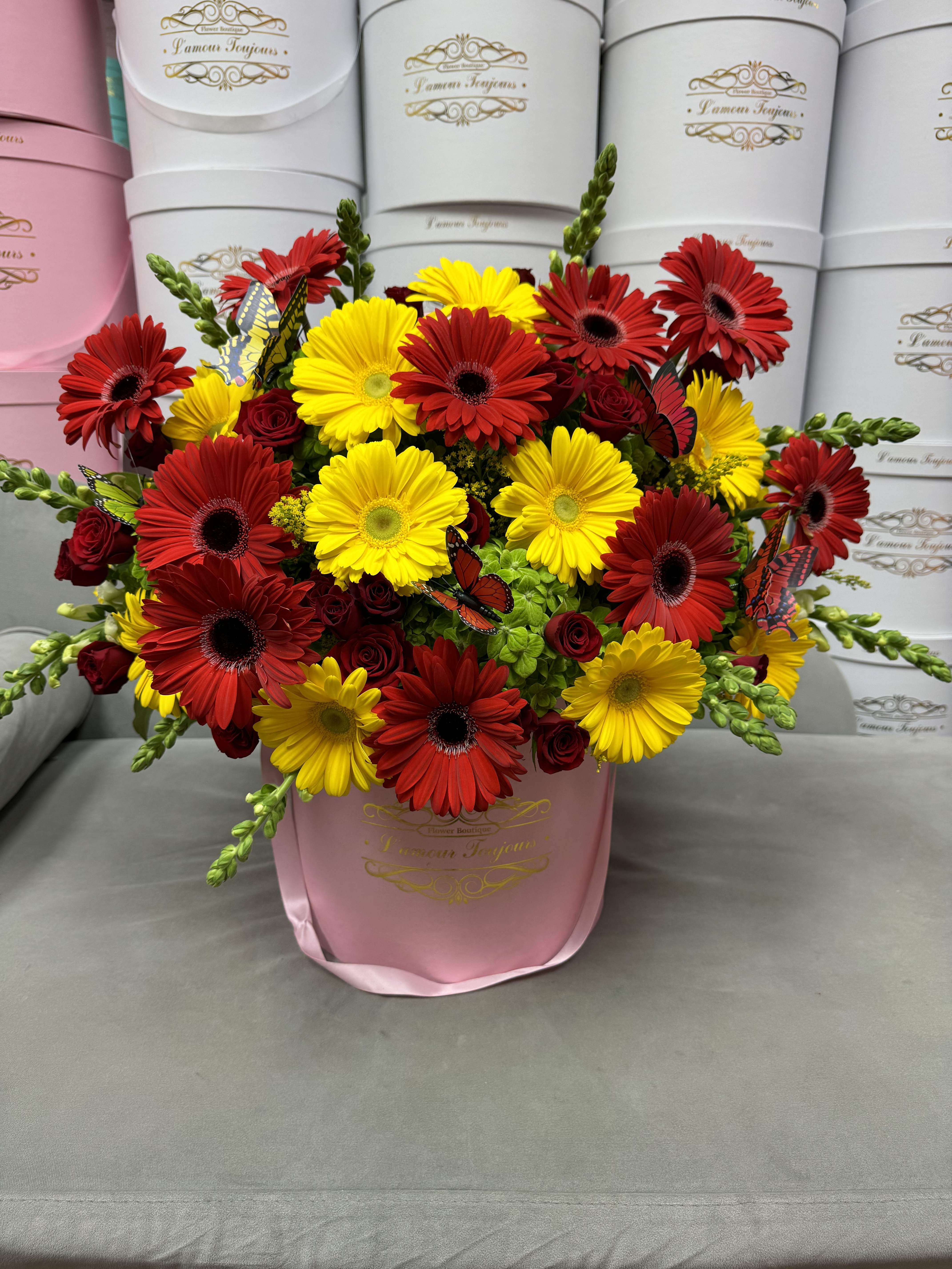 Bouquet of red and yellow daisies in a pink hatbox