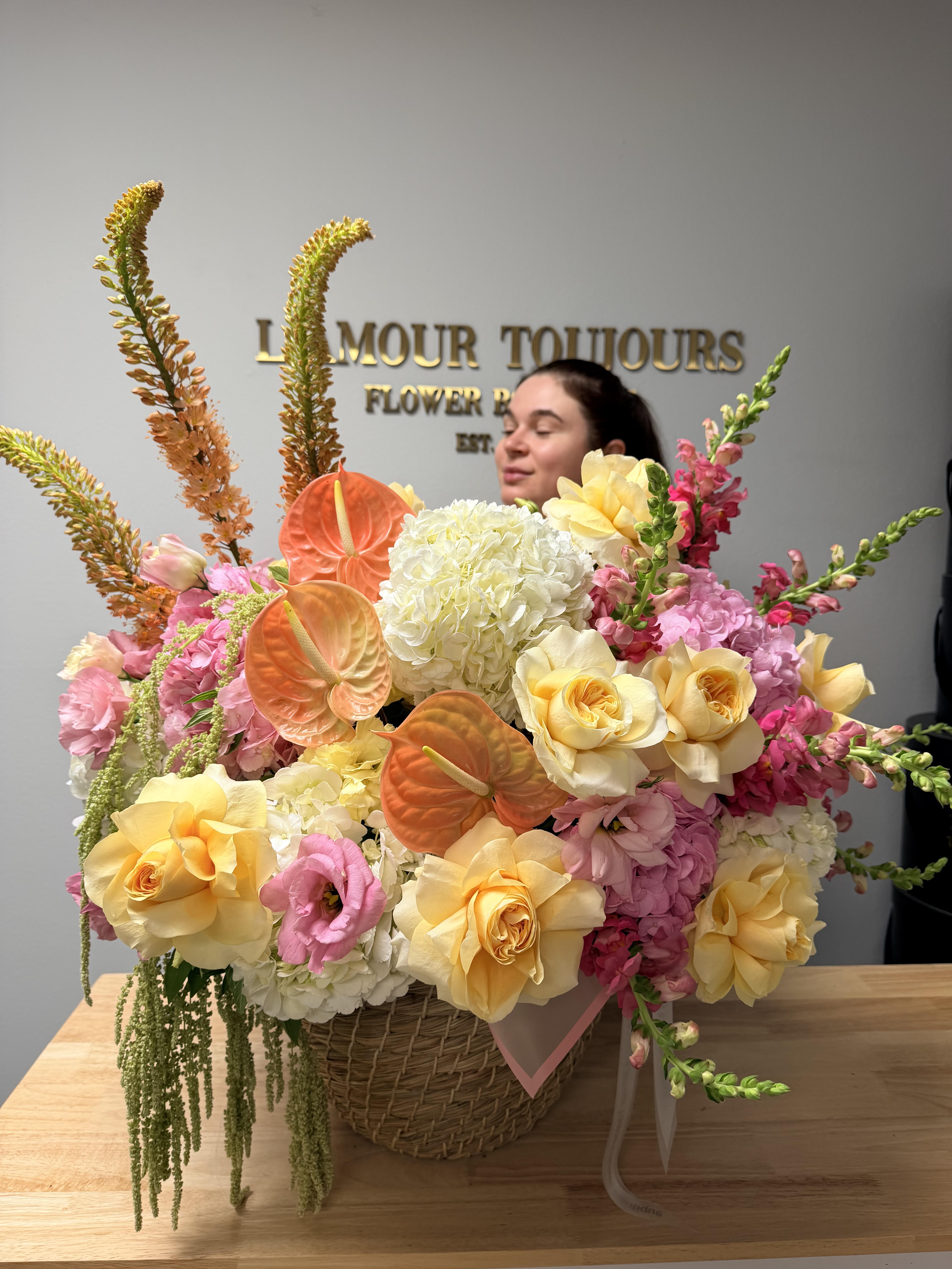 Large pastel flower arrangement in a wicker basket with roses and anthuriums