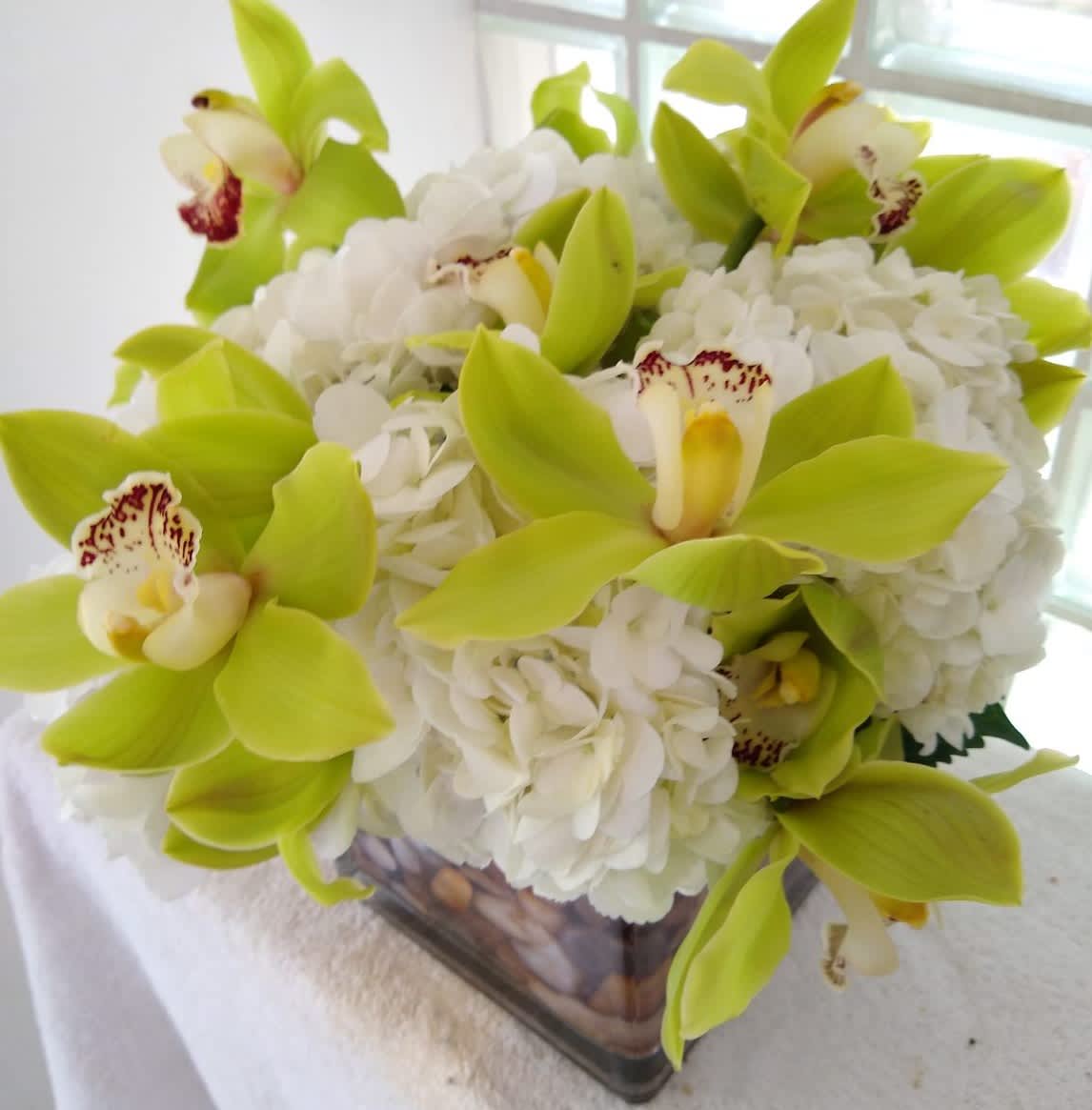 White hydrangeas with lime green orchids in a square glass vase