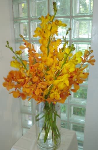 Tall yellow and orange orchid arrangement in a clear glass vase