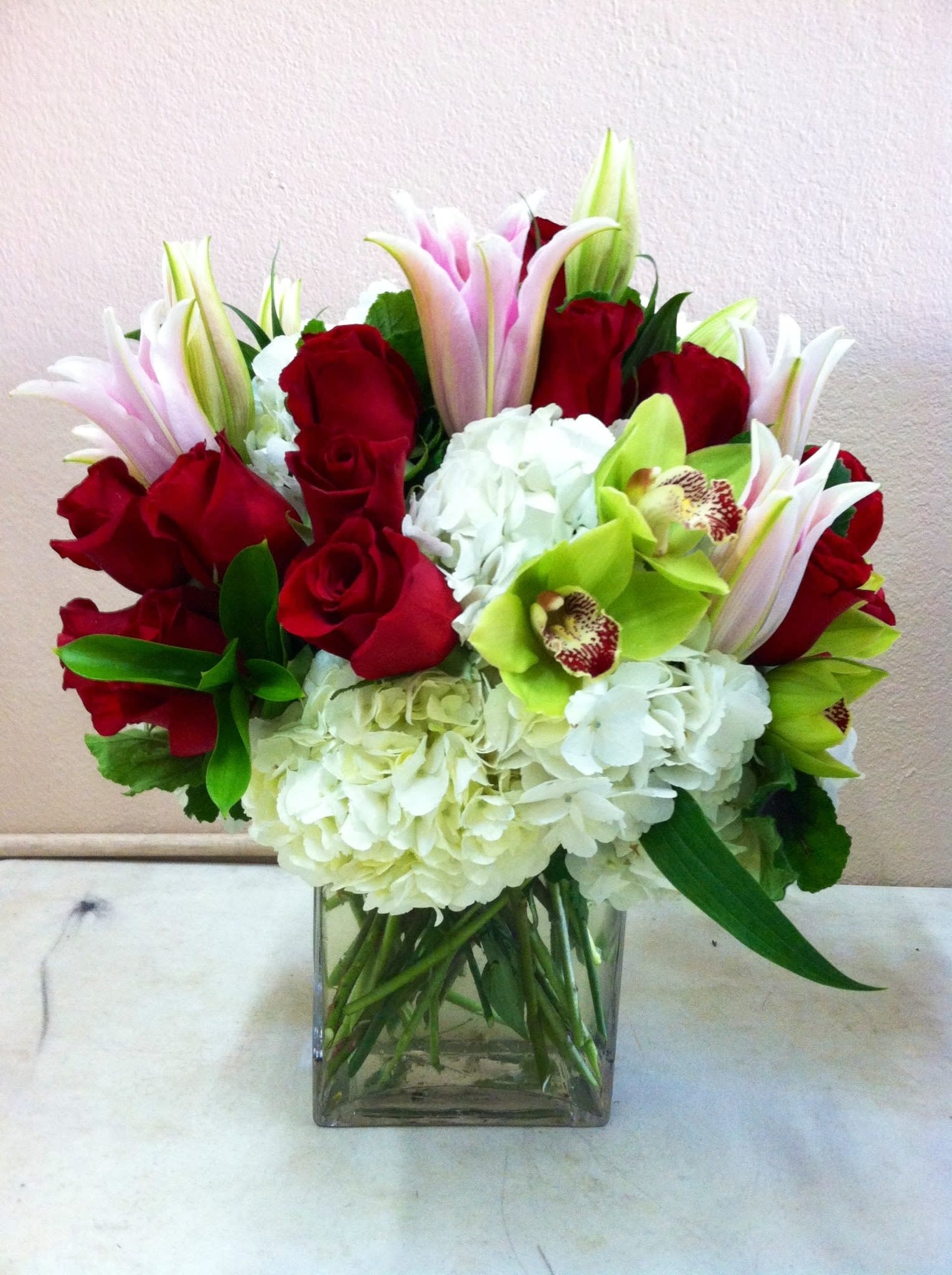 Bouquet of red roses, white hydrangeas, and green orchids in a glass vase