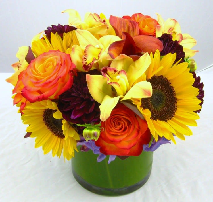 Bouquet of sunflowers, orange roses, and yellow calla lilies in a green vase