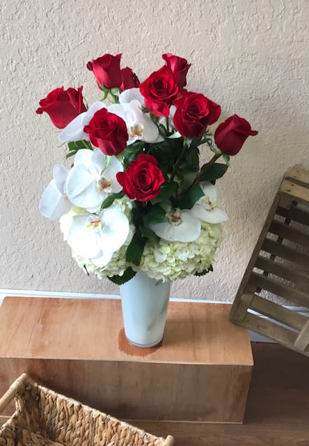 Red roses and white orchids arranged in a tall white vase