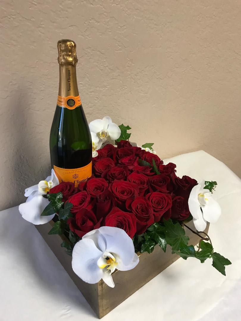 Red roses arranged with white orchids and a champagne bottle