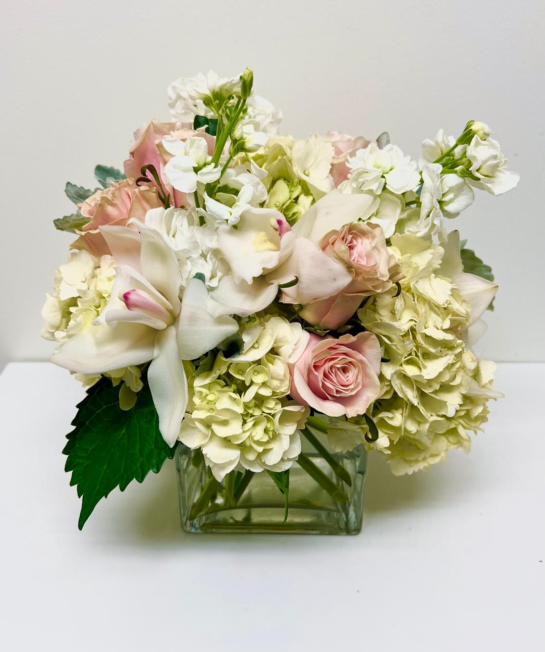 Pink roses and white lilies arranged in a square glass vase