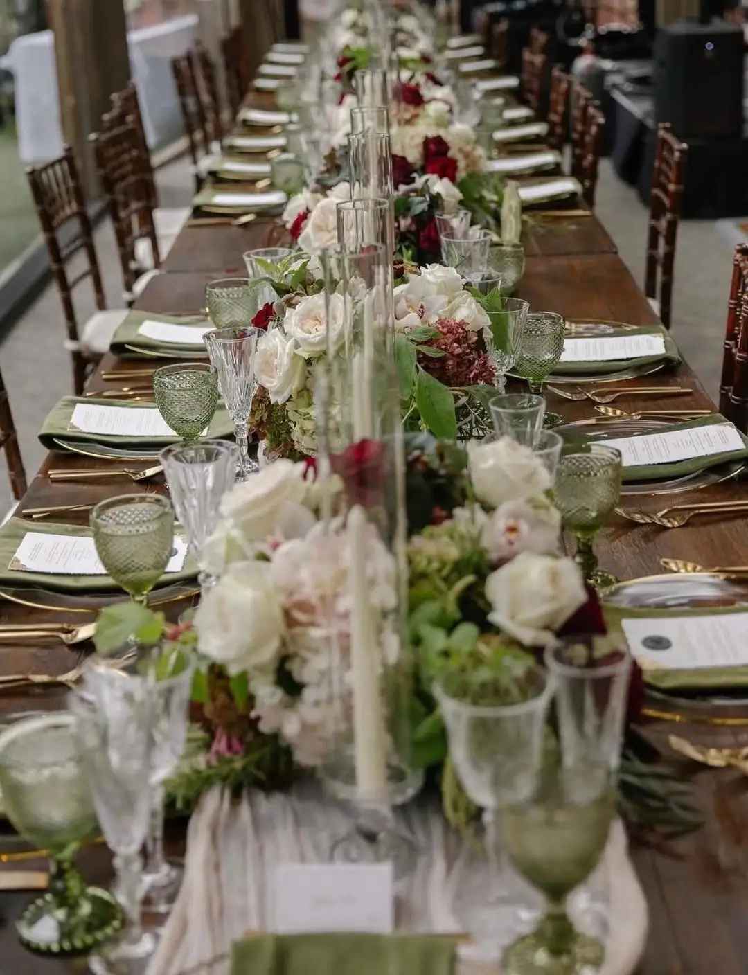 Long banquet table with white and red floral centerpieces in glass vases
