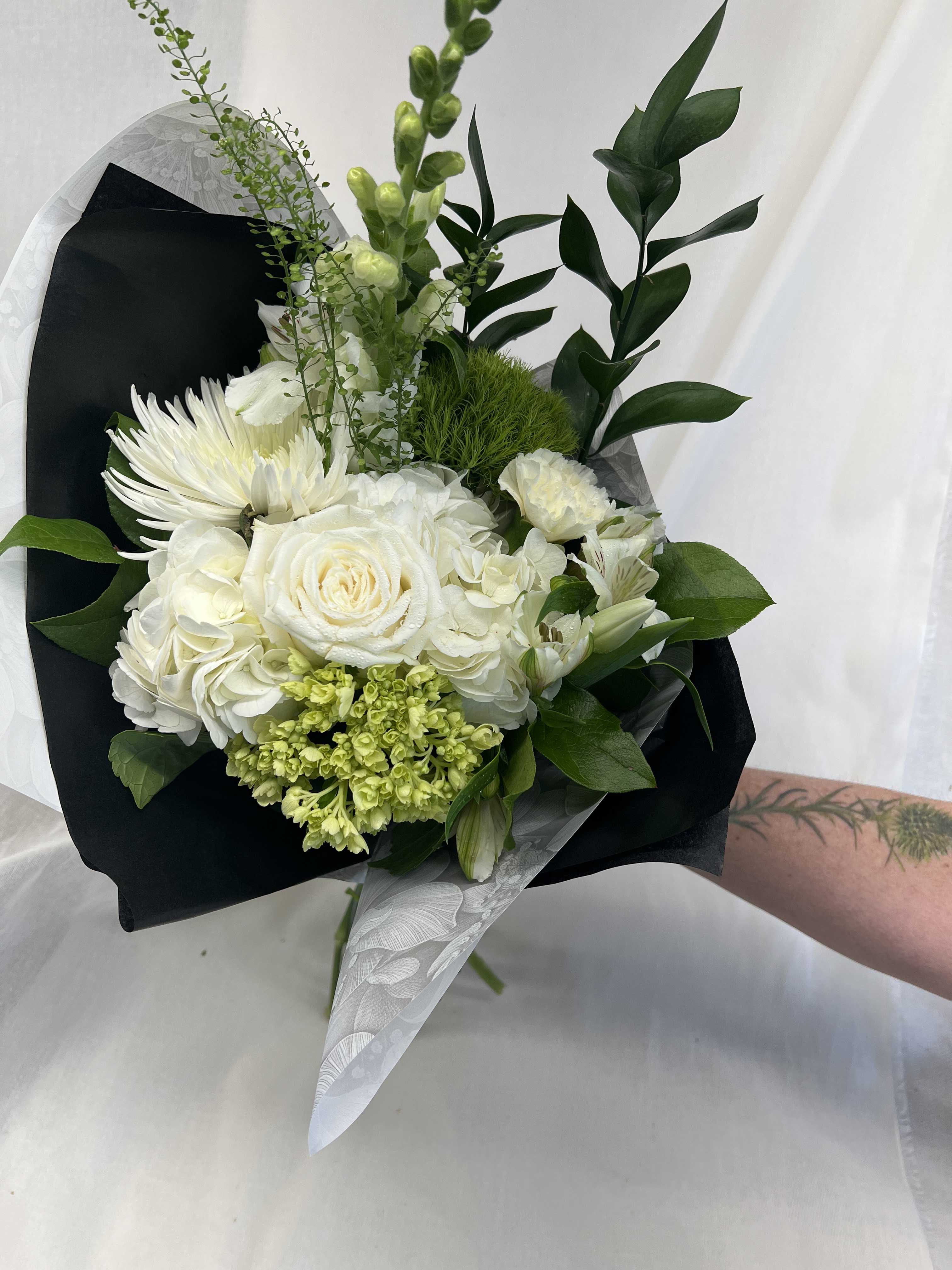 White bouquet with roses, hydrangeas, and chrysanthemums wrapped in black paper