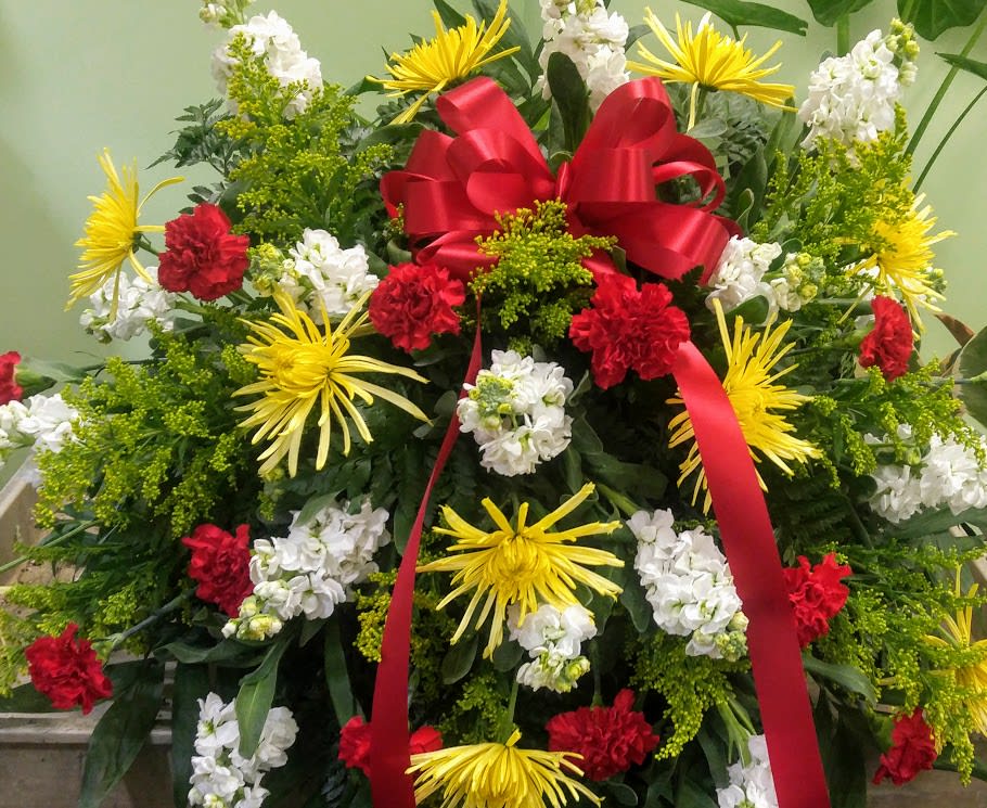 Large standing floral spray with red ribbon and yellow, white, and red flowers