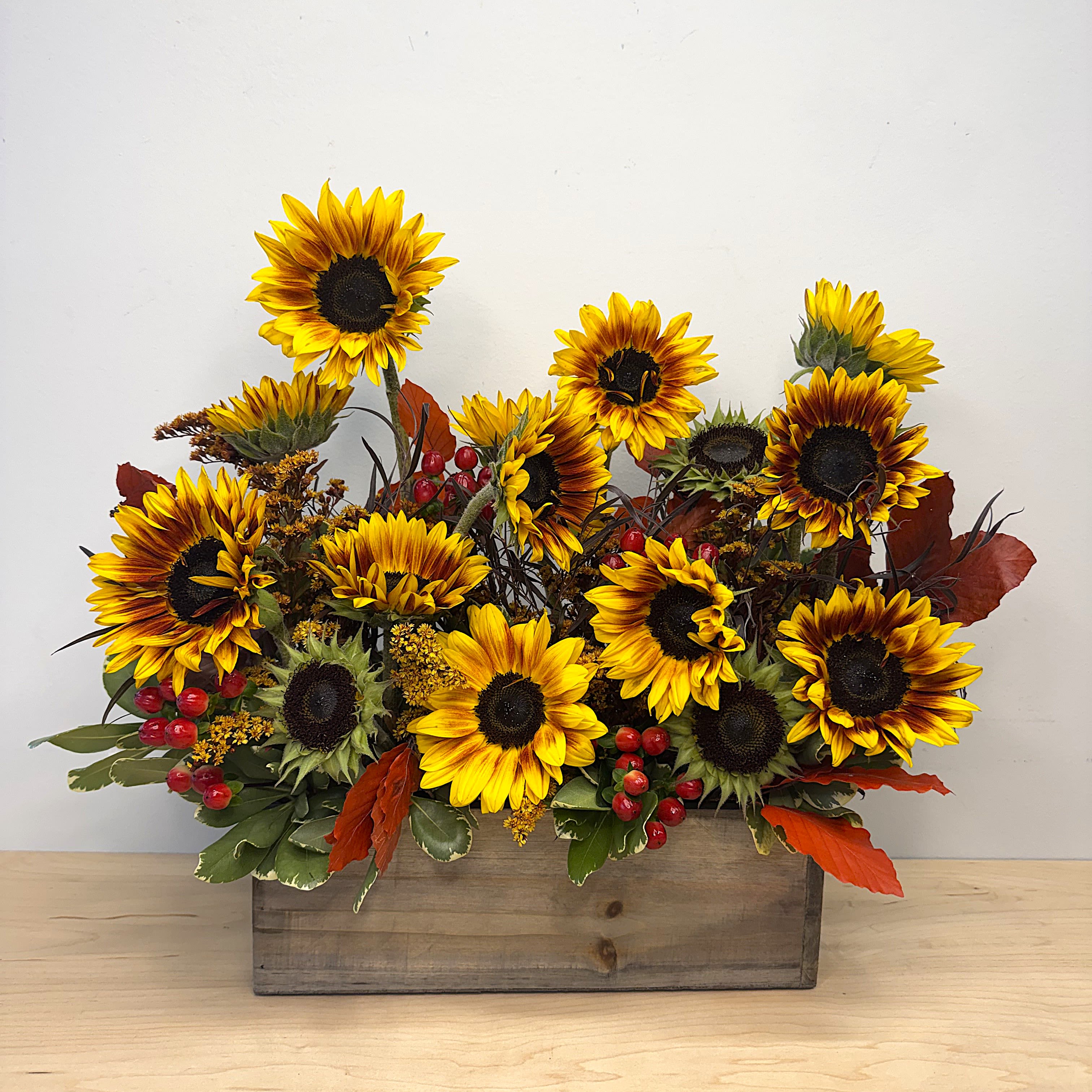 Sunflower arrangement in a wooden box with red berries and autumn leaves