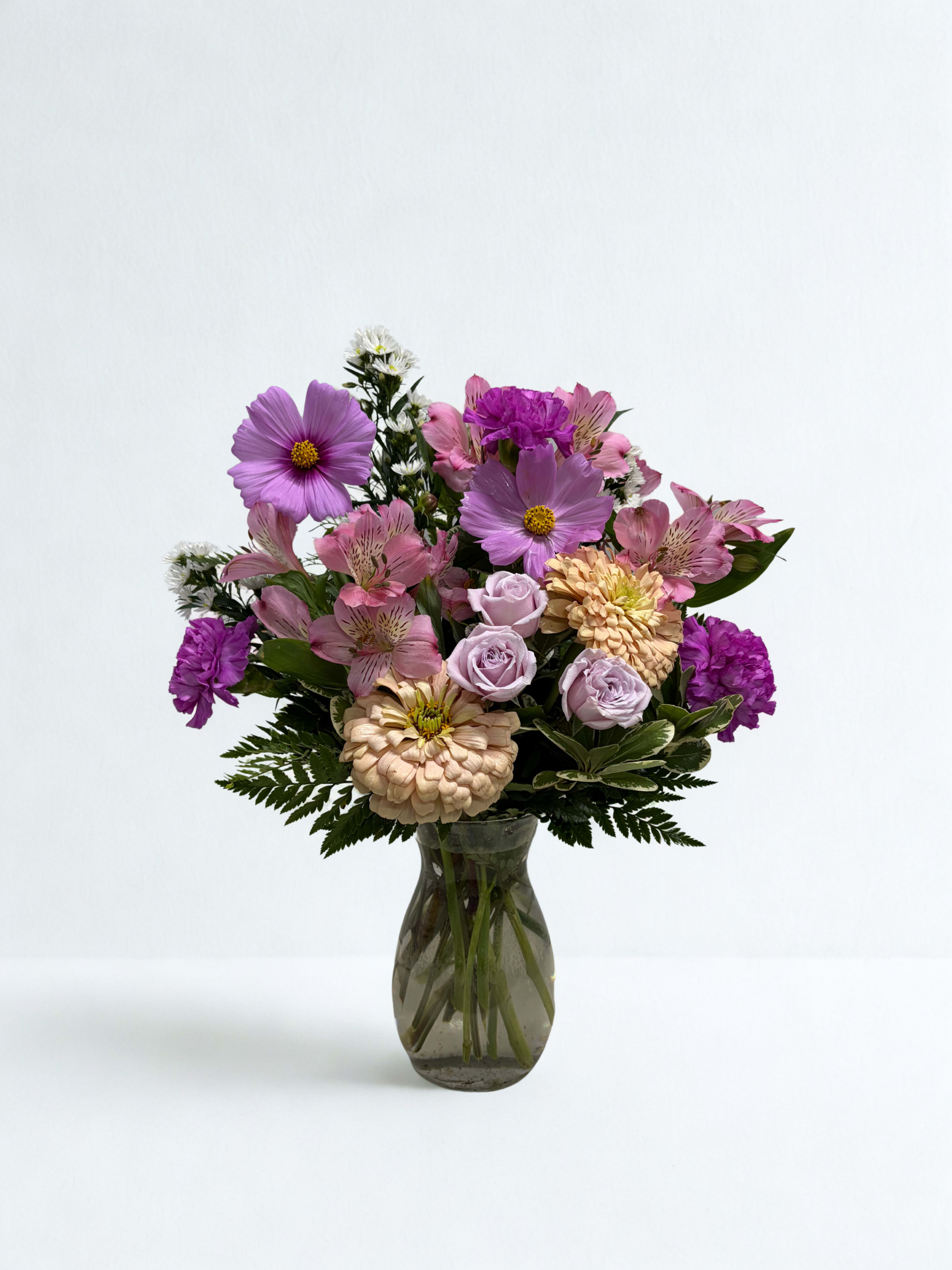 Mixed pink and purple flowers arranged in a glass vase