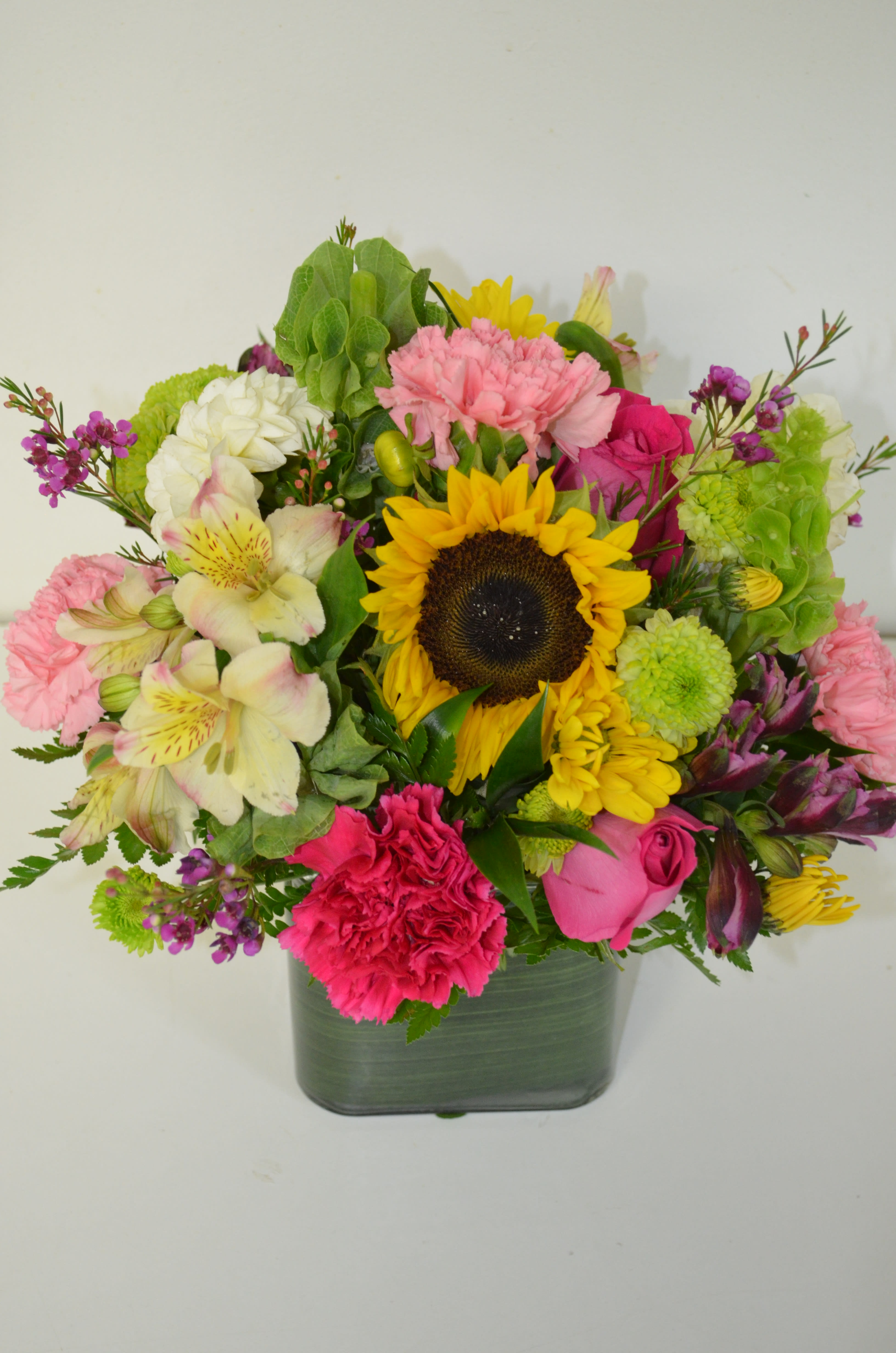 Mixed bouquet with a sunflower, pink carnations, and roses in a glass vase