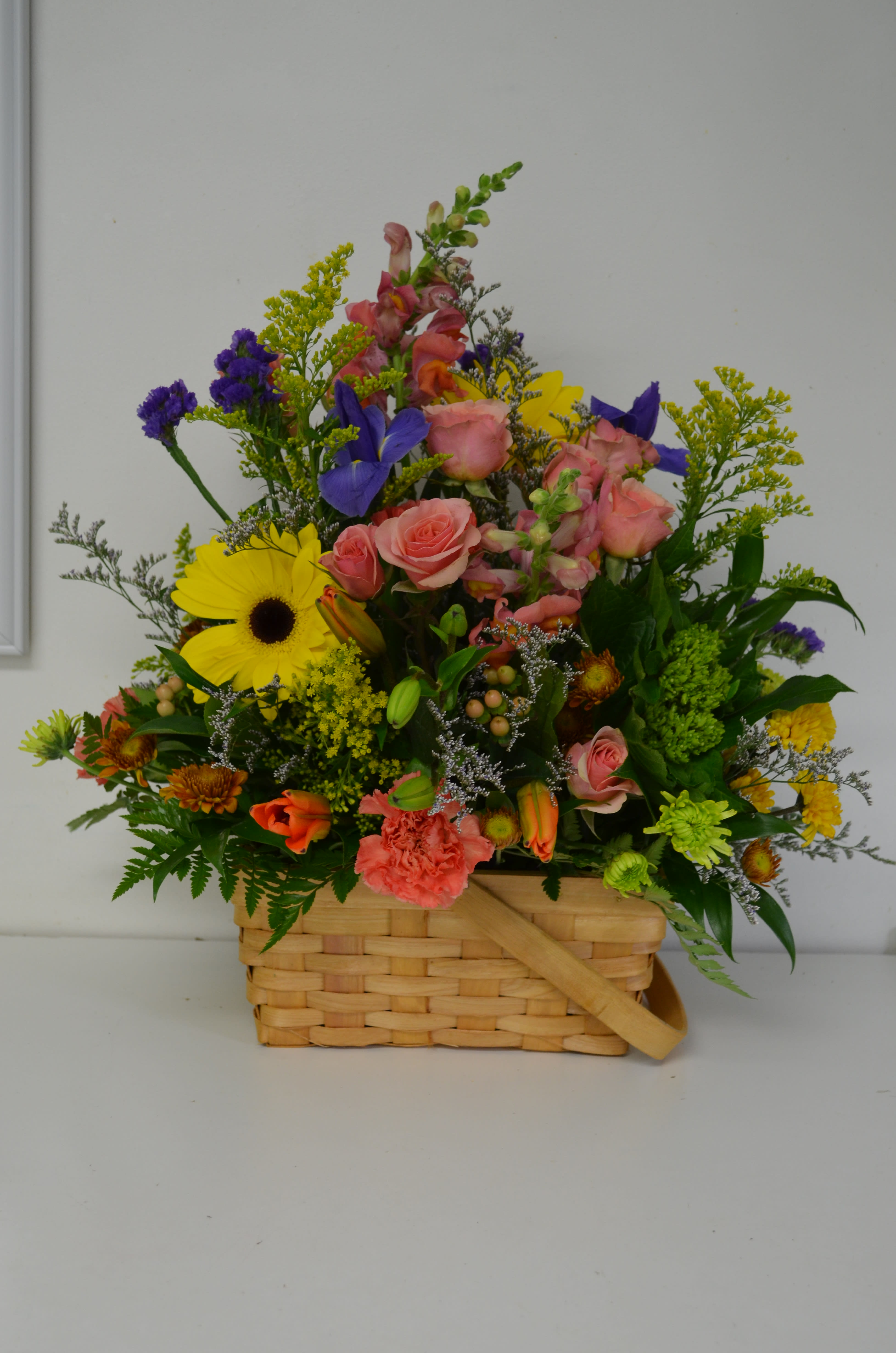 Mixed flower arrangement in a woven basket with pink, yellow, and purple blooms