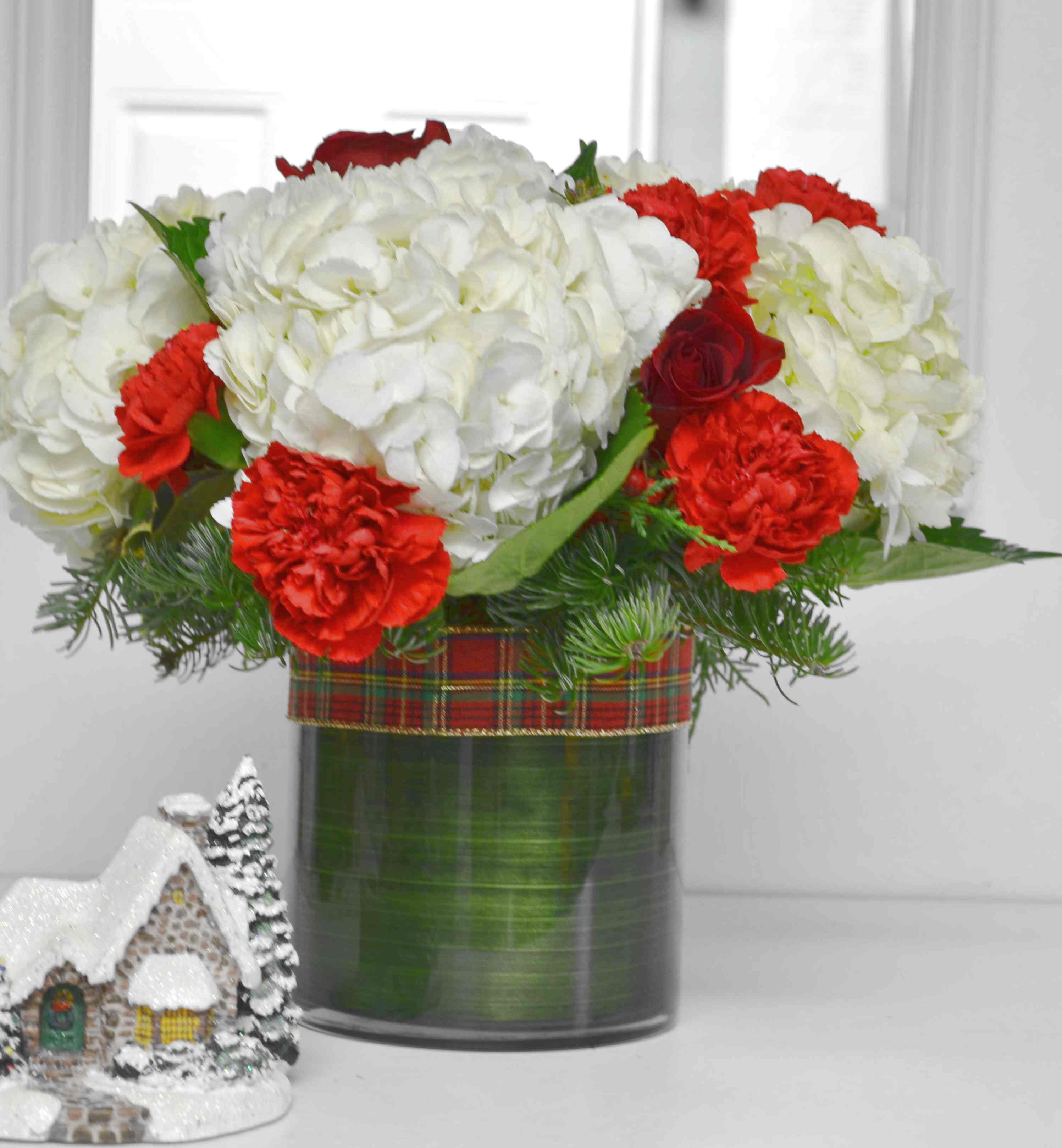 White hydrangeas and red carnations in a glass vase with plaid ribbon
