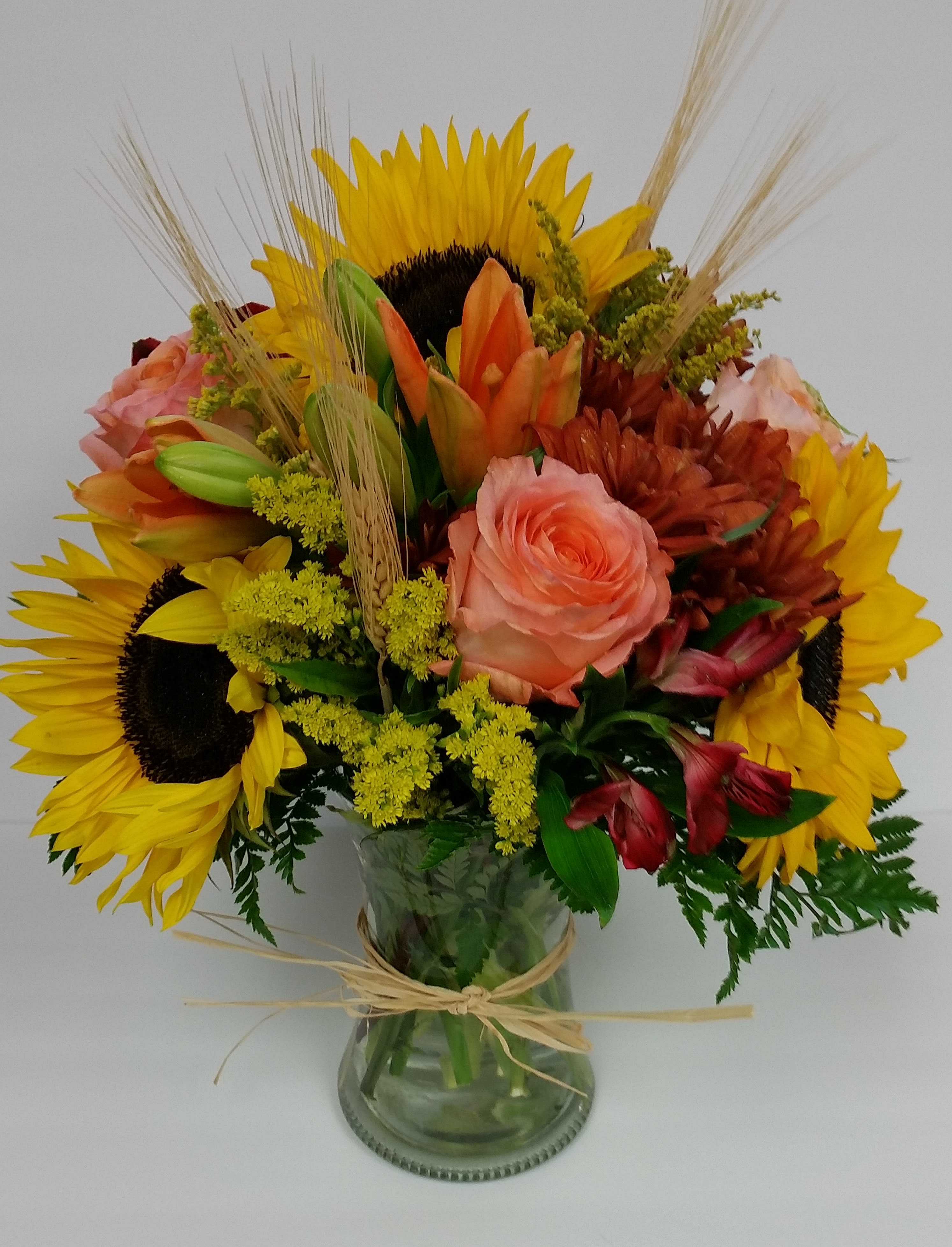 Bouquet of sunflowers, roses, and lilies in a glass vase
