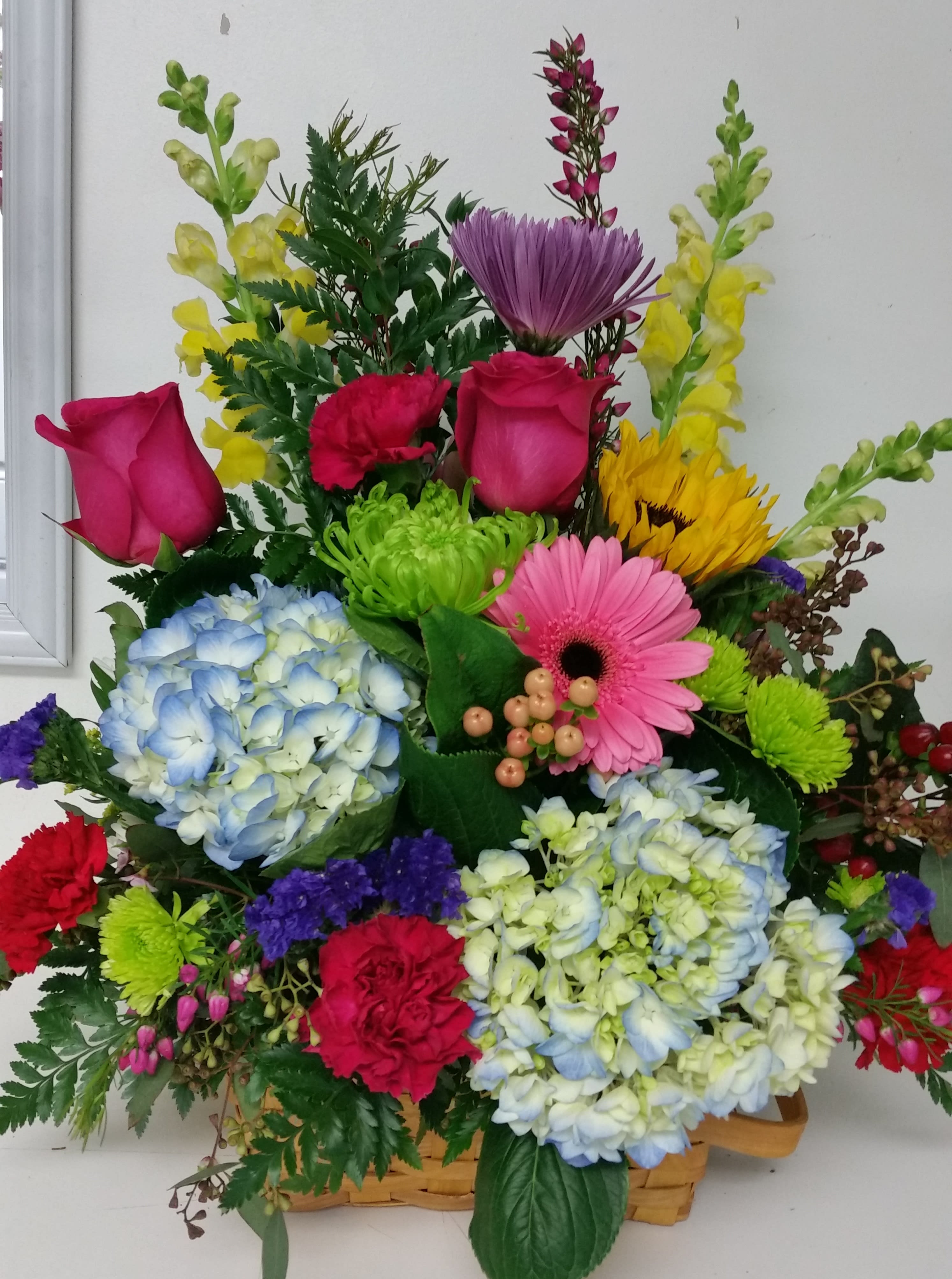 Colorful mixed flower arrangement in a basket with roses, hydrangeas, and gerbera daisies