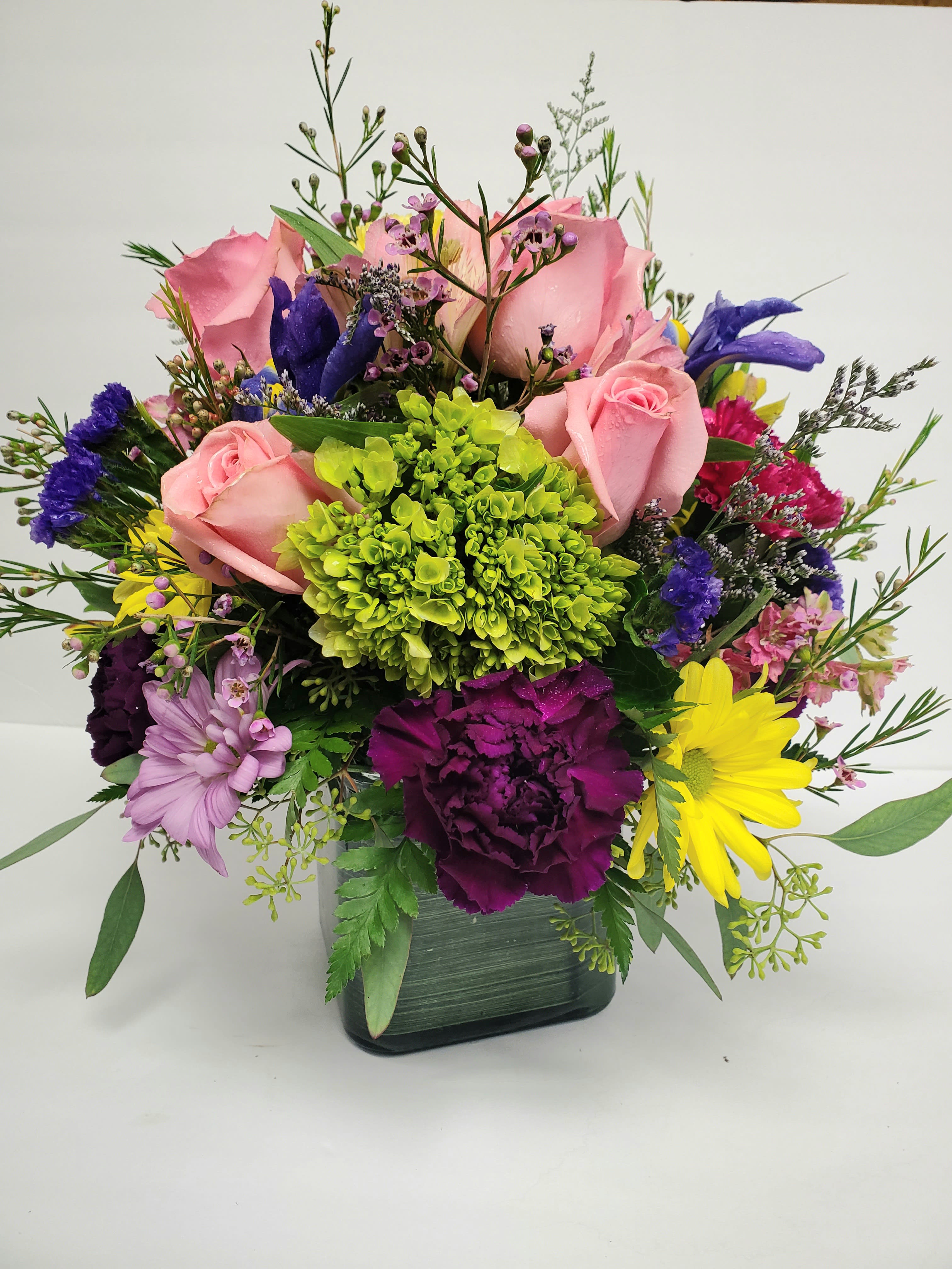 Mixed bouquet of pink roses, daisies, and colorful filler flowers in a square vase