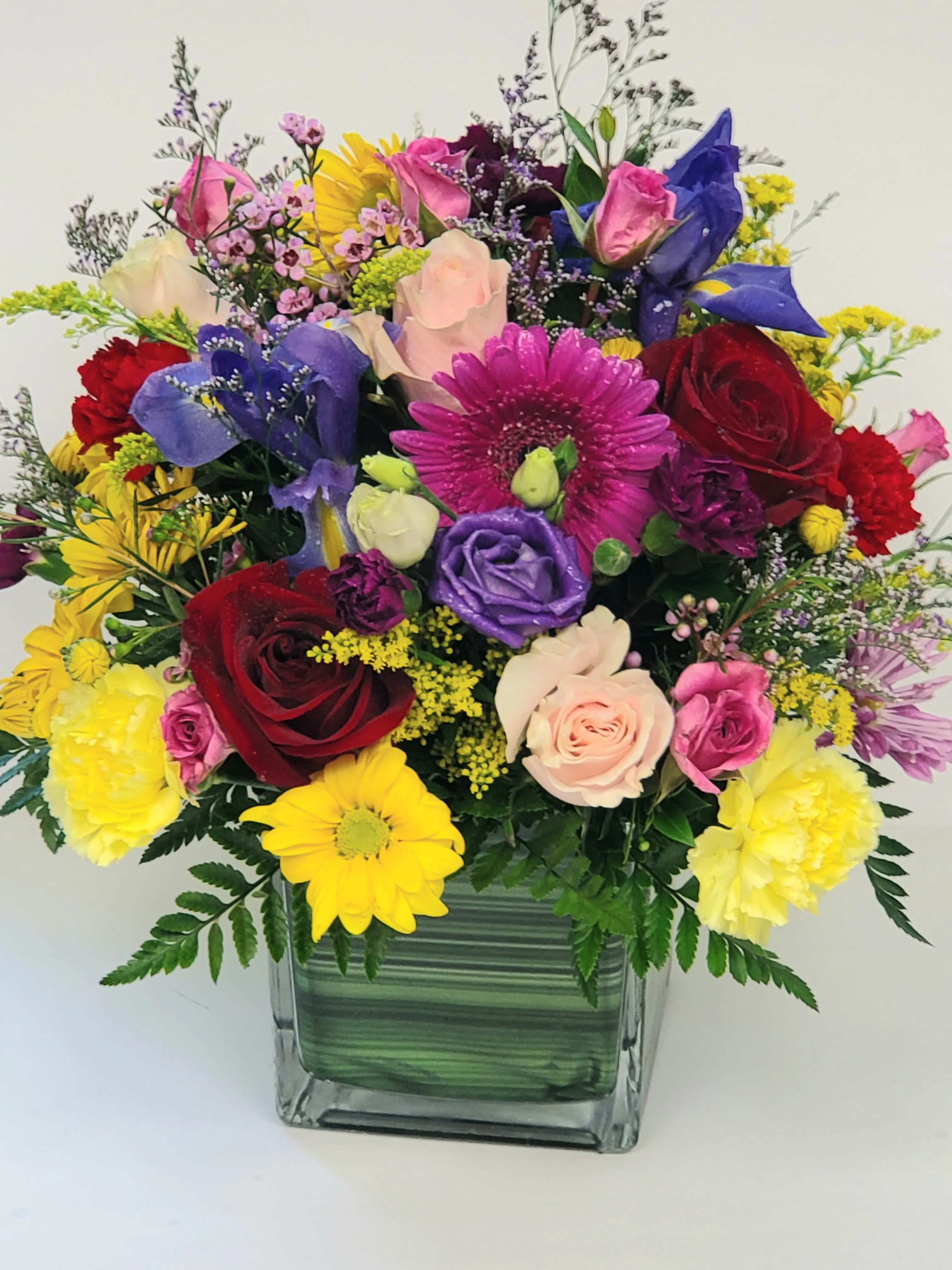 Mixed bouquet in a square glass vase with roses, daisies, and colorful blooms