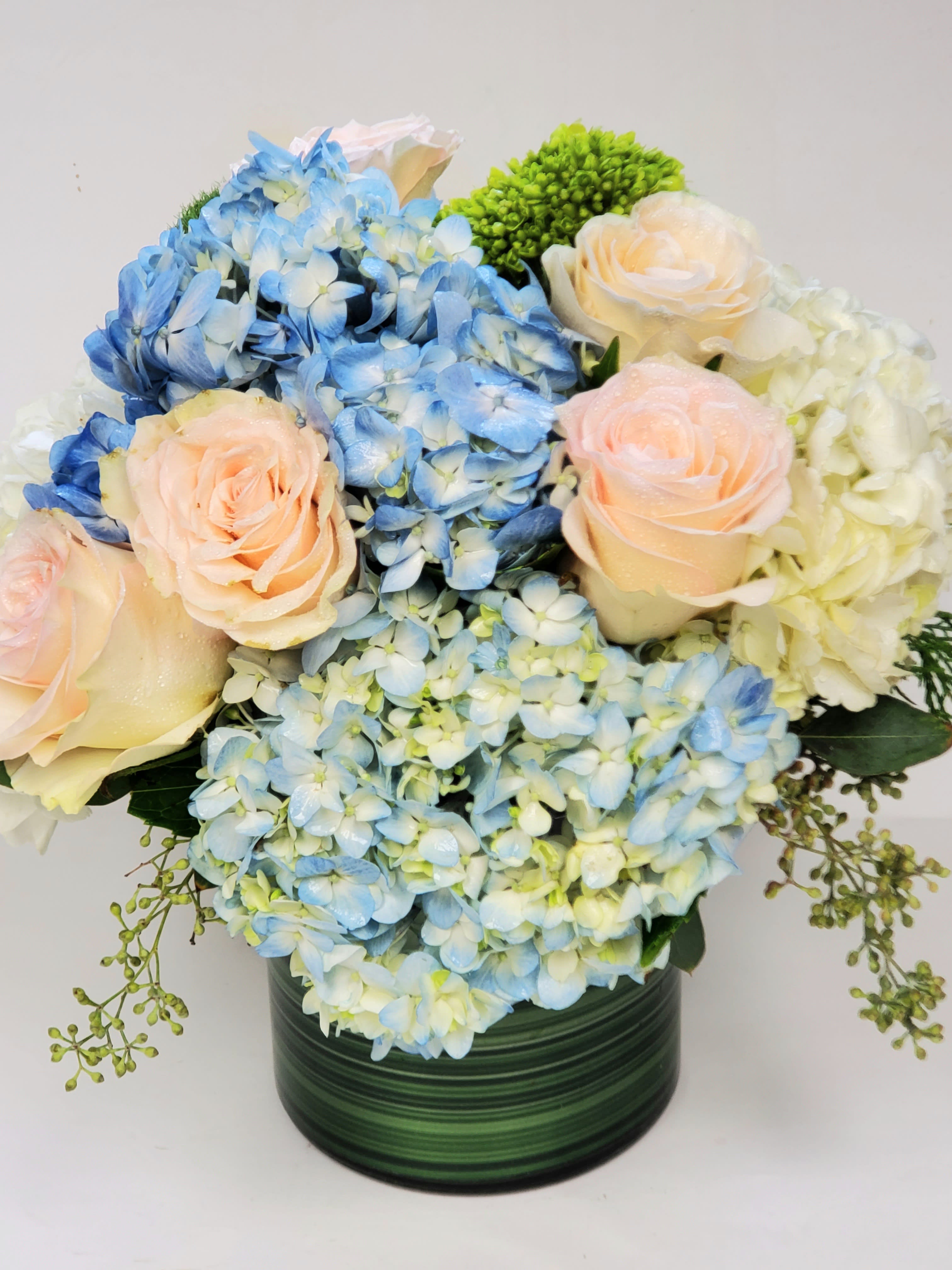 Blue hydrangeas and pale roses arranged in a green vase