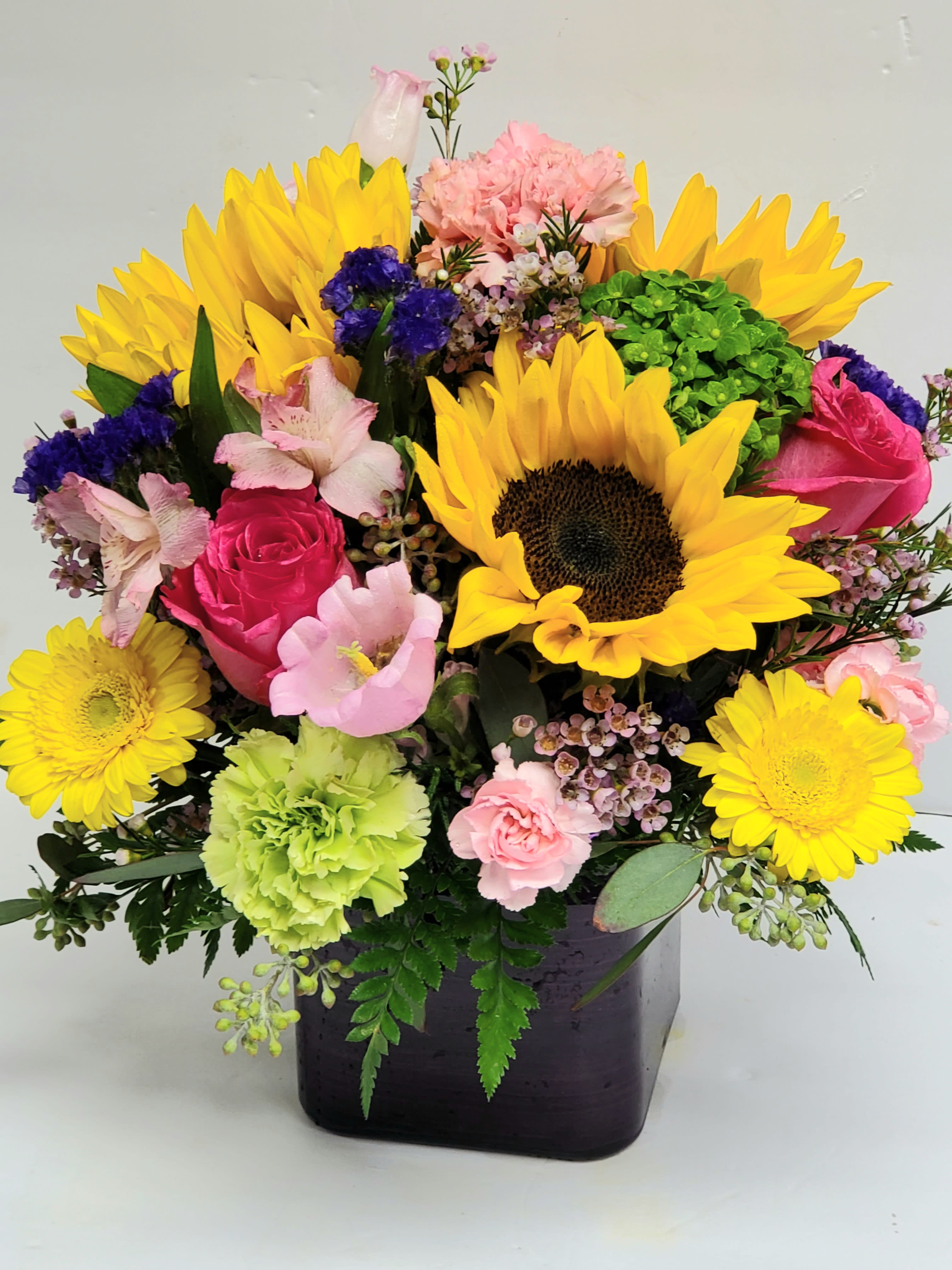 Bright mixed bouquet with sunflowers, pink roses, and carnations in a dark vase