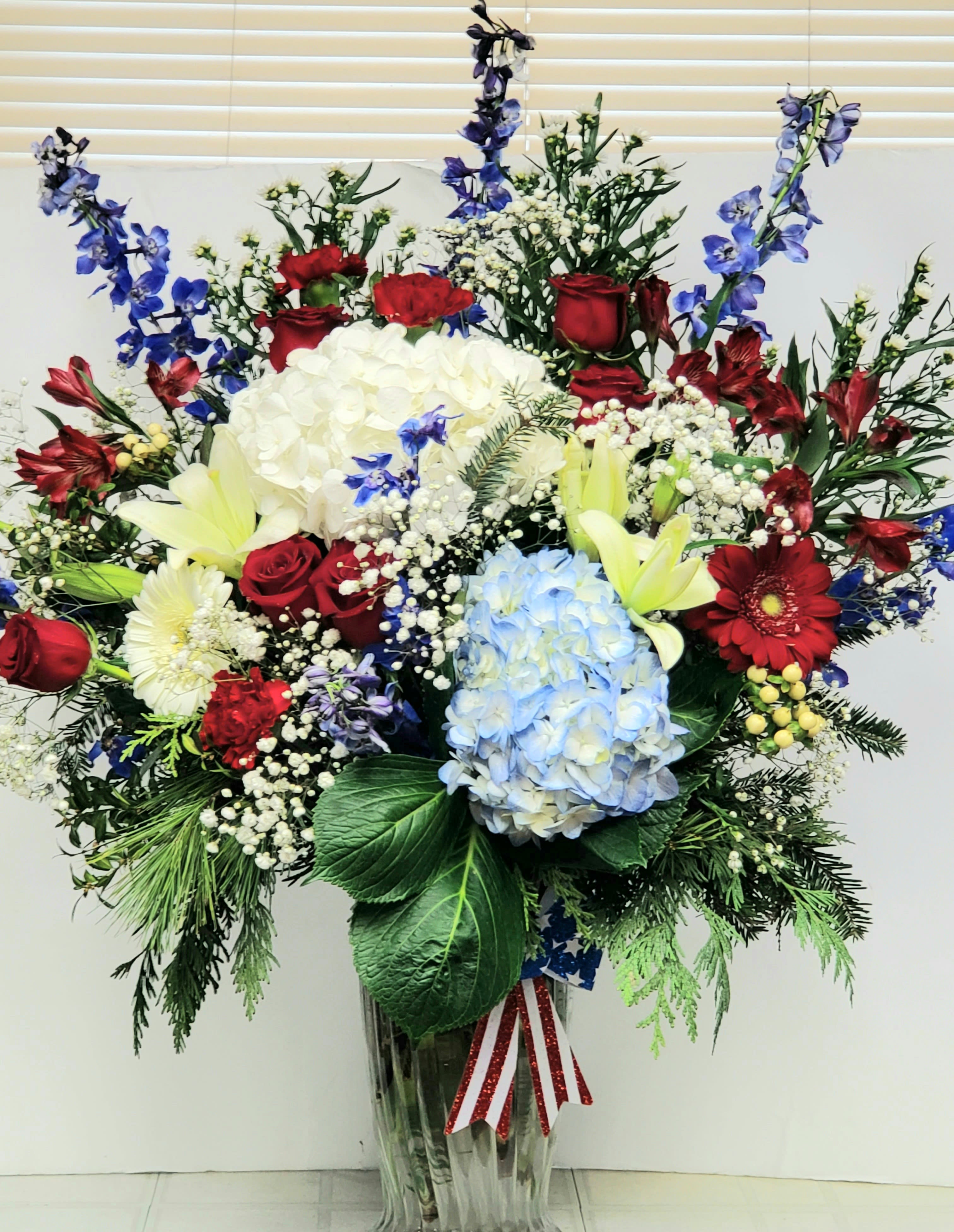 Large mixed floral arrangement in a clear vase with red, white, blue, and yellow blooms