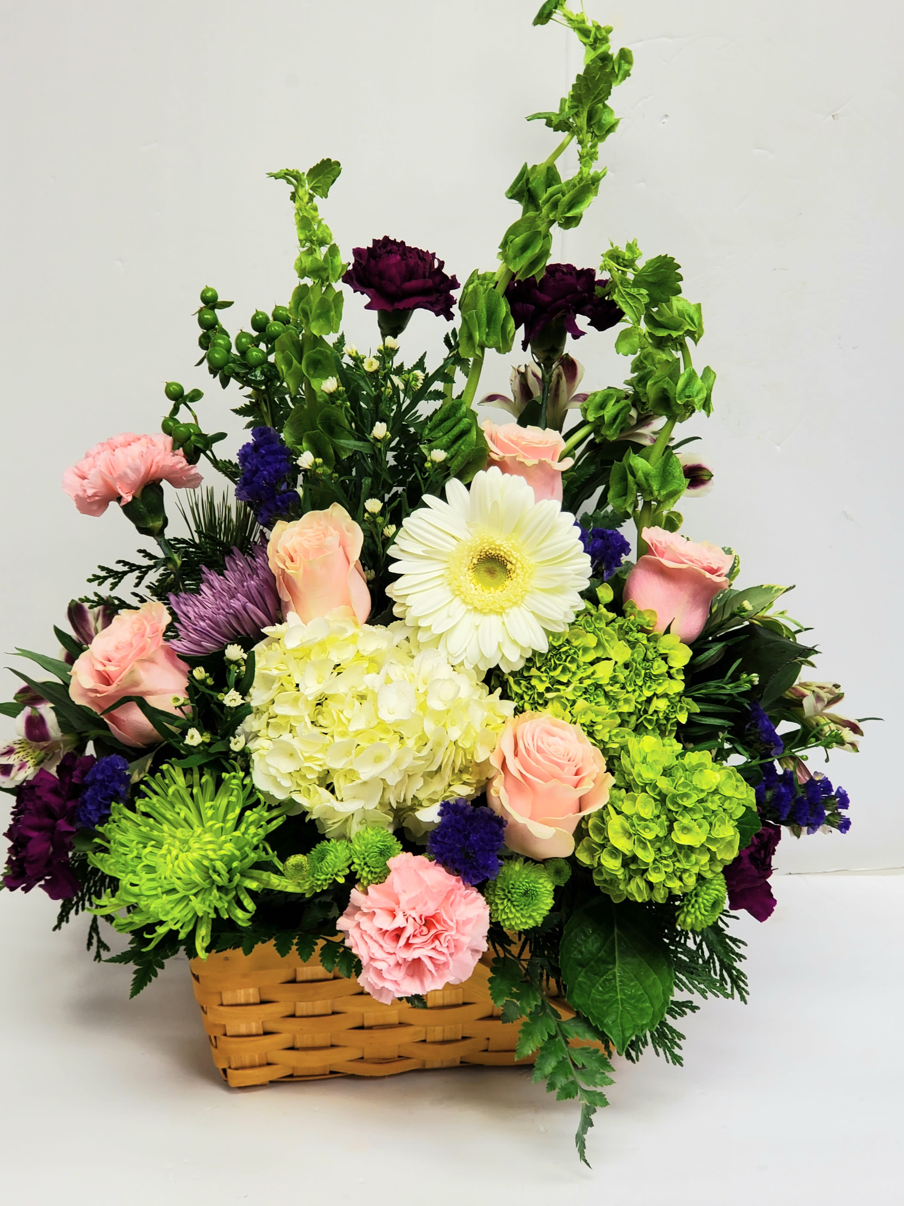 Basket arrangement of pink roses, white gerbera, hydrangea, and purple flowers