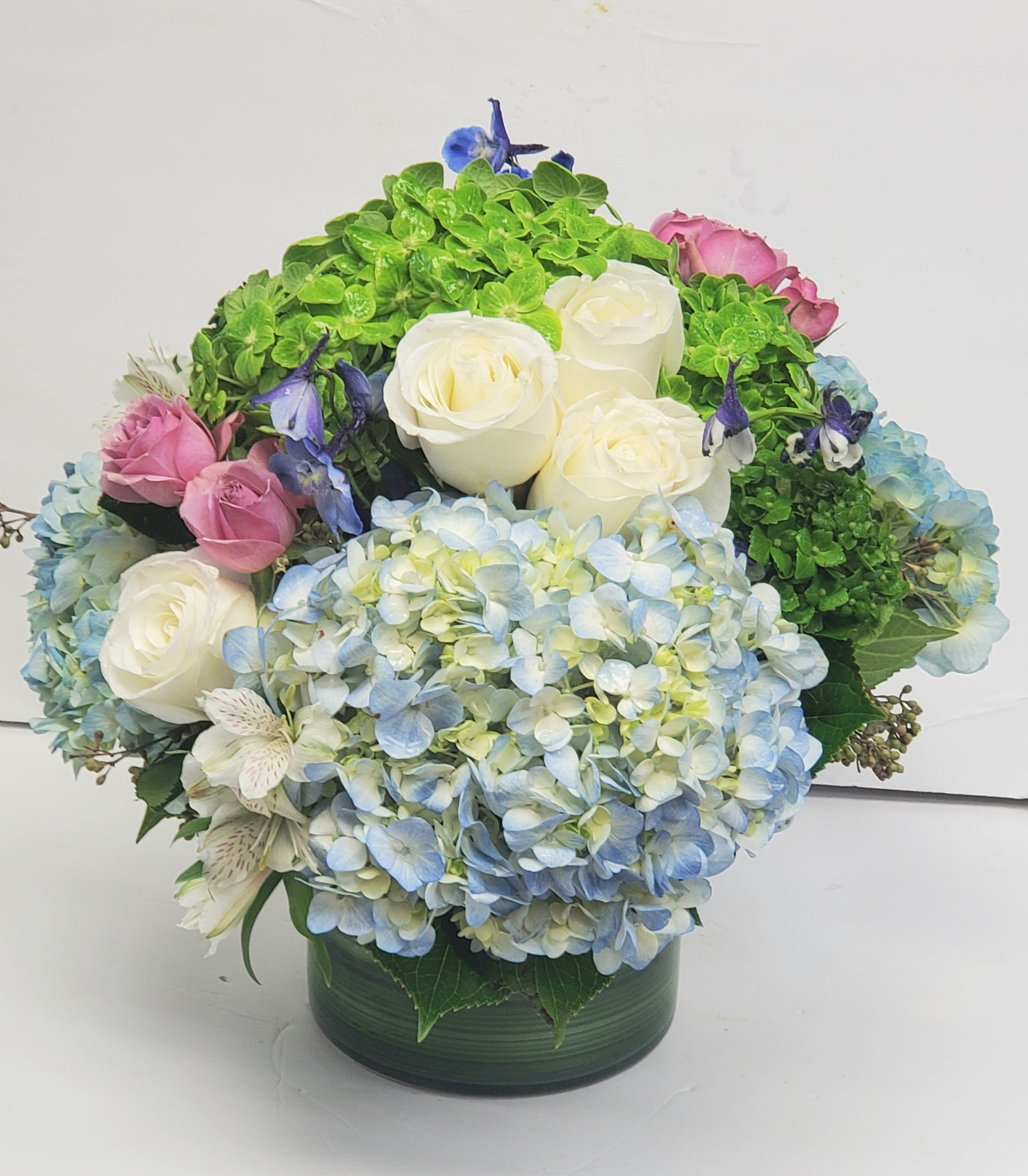 Bouquet of white roses, blue hydrangeas, and pink roses in a green vase