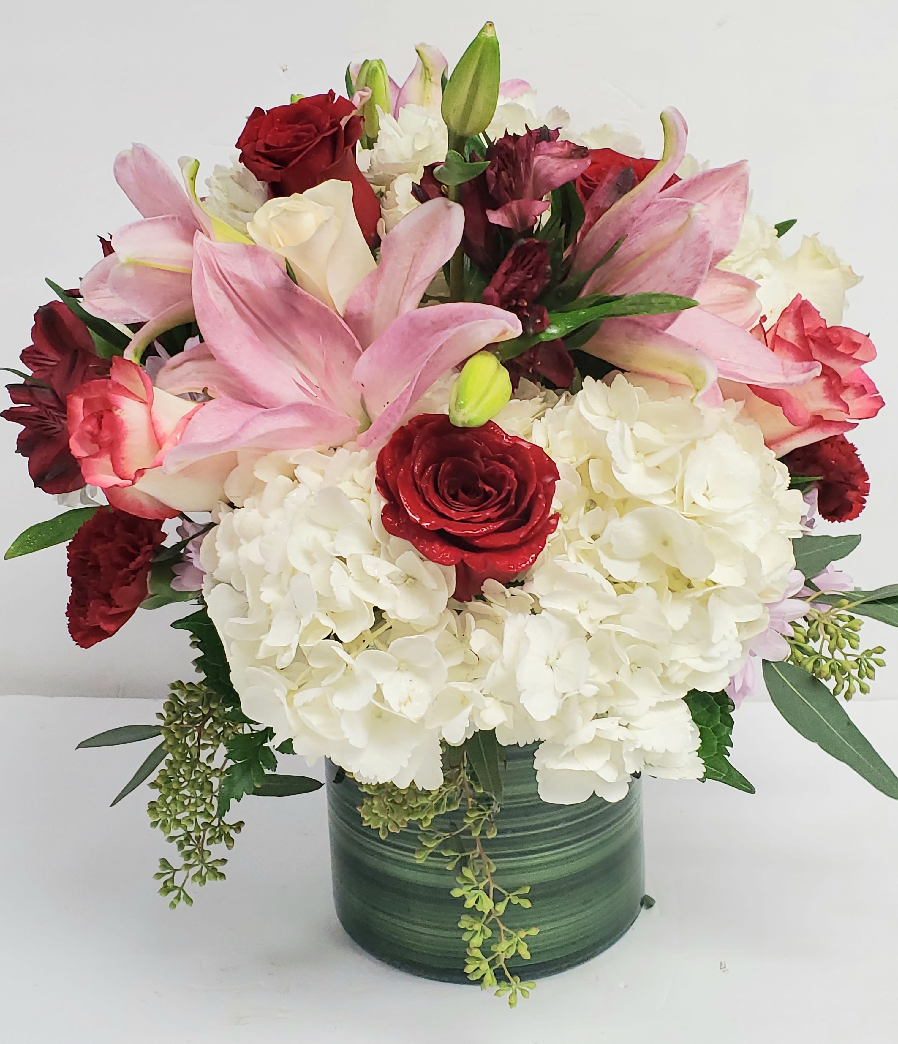 Bouquet of pink lilies, red roses, and white hydrangeas in a green vase