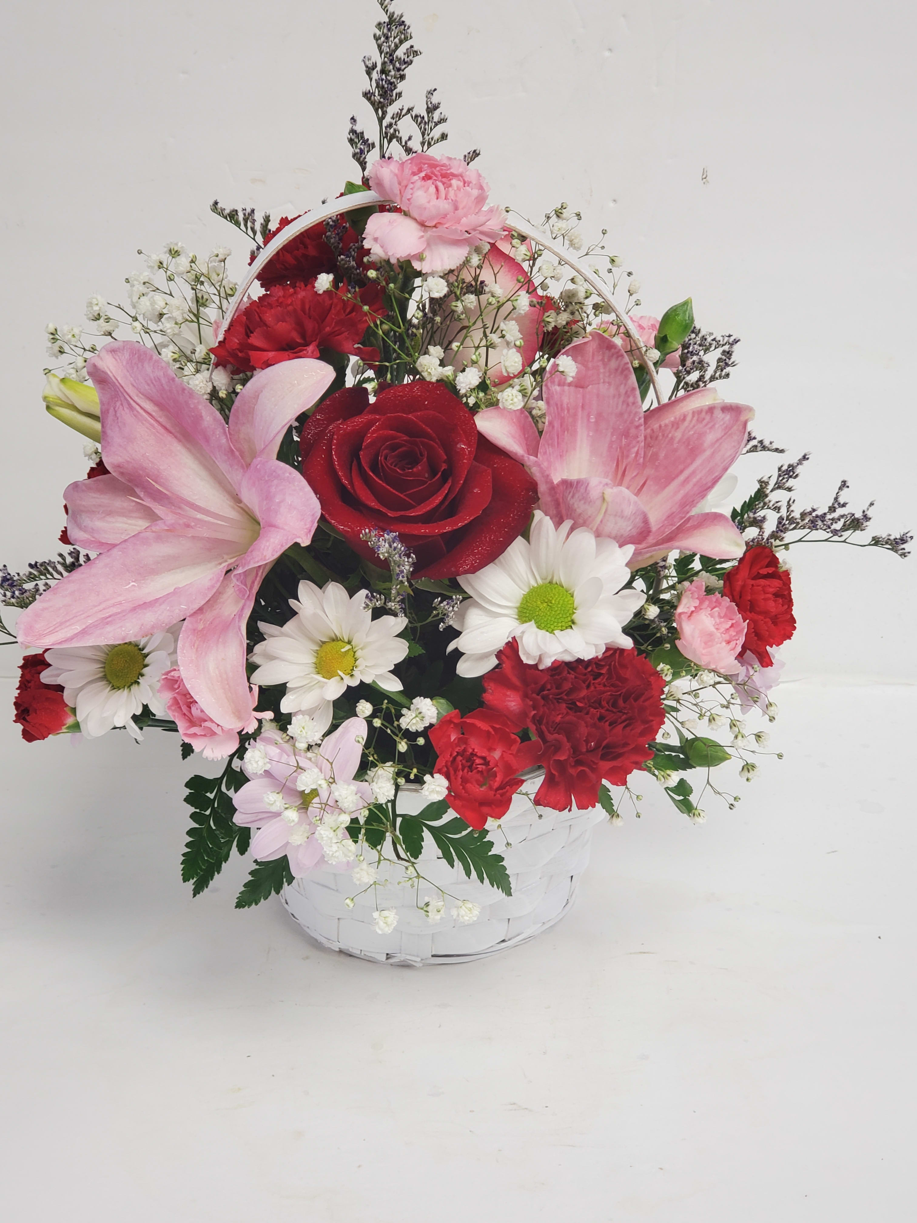 Basket arrangement of red roses, pink lilies, and white daisies