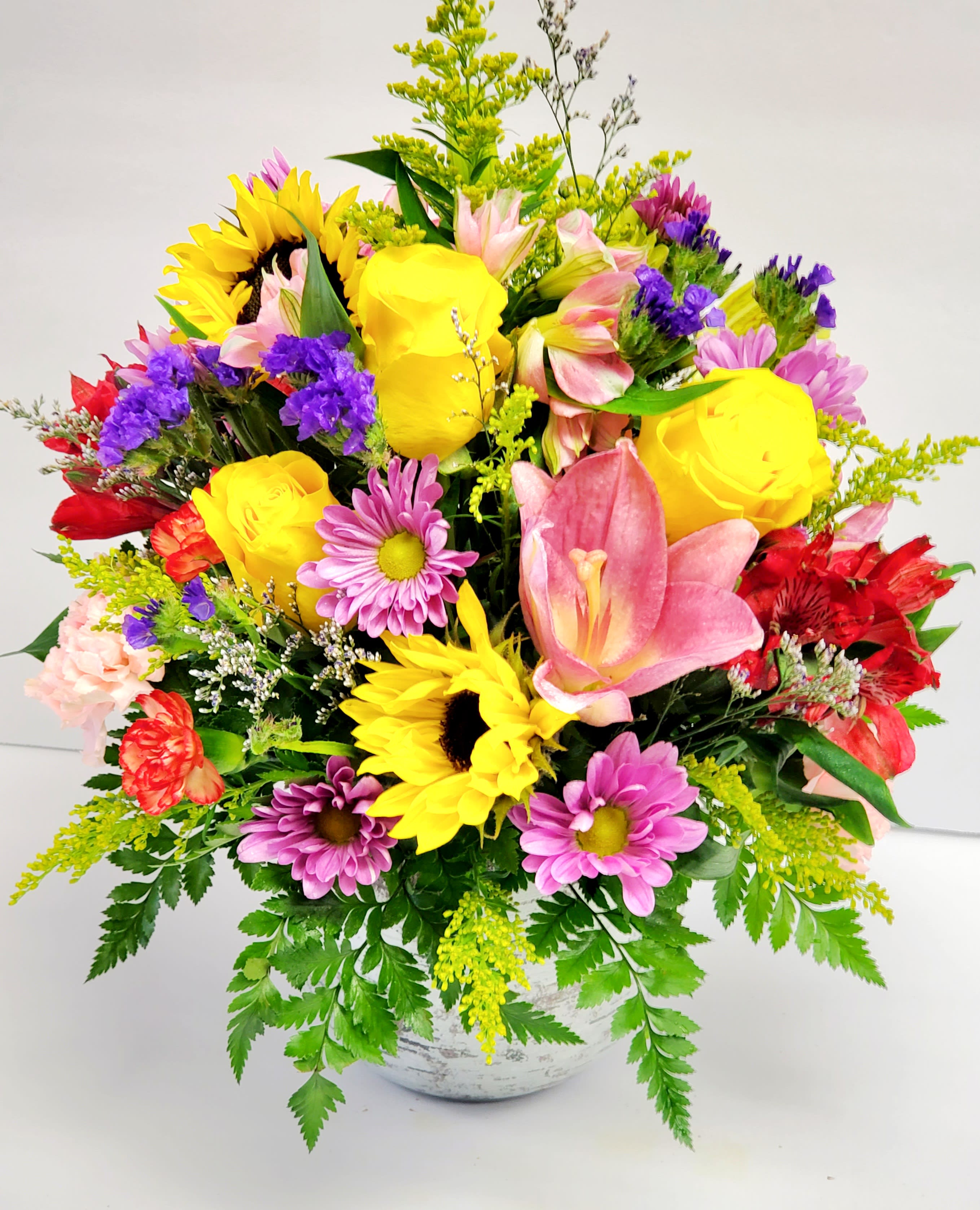 Colorful mixed bouquet with sunflowers, roses, lilies, and daisies in a white vase