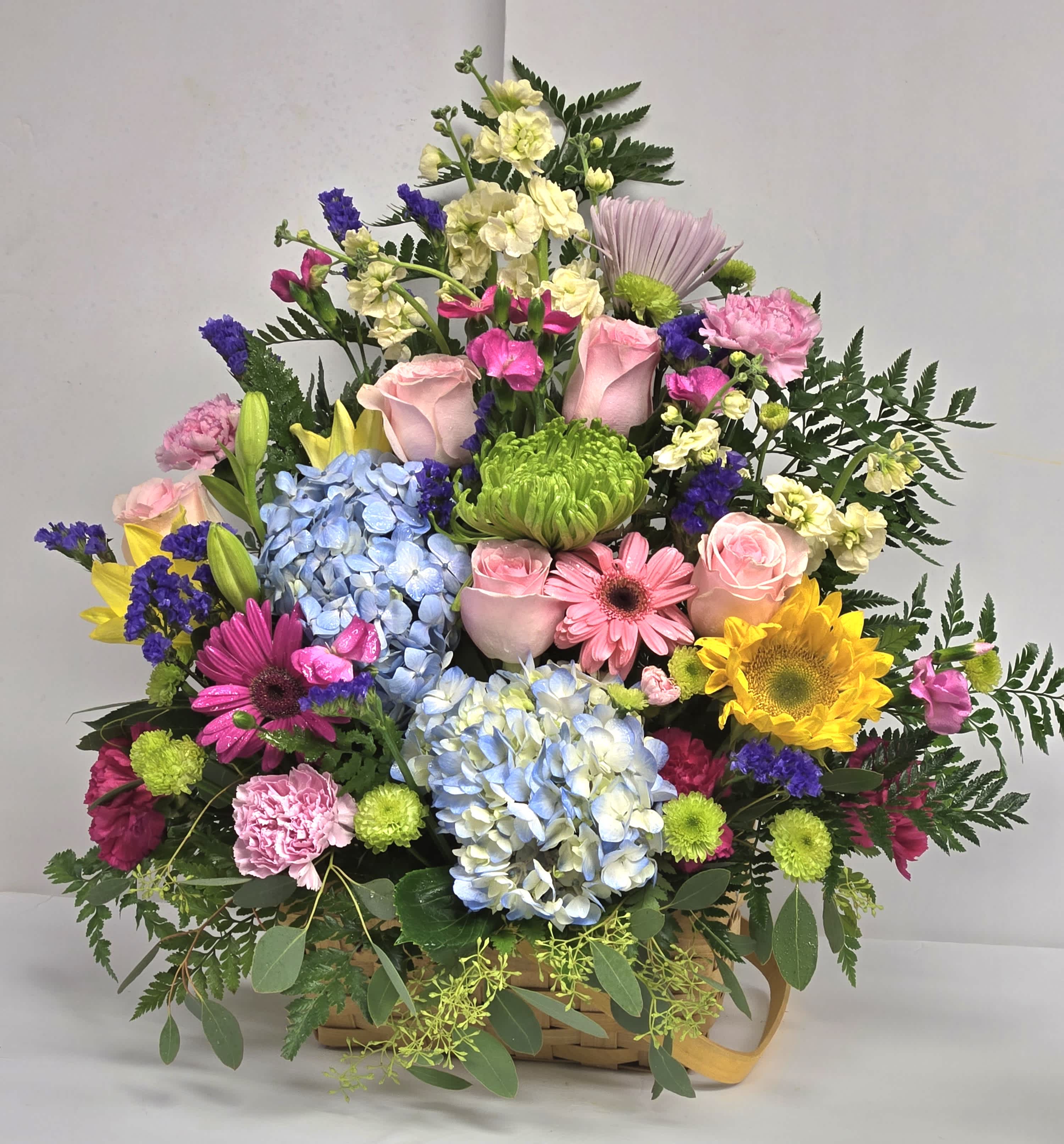 Colorful mixed flower arrangement in a basket with roses, hydrangeas, and daisies