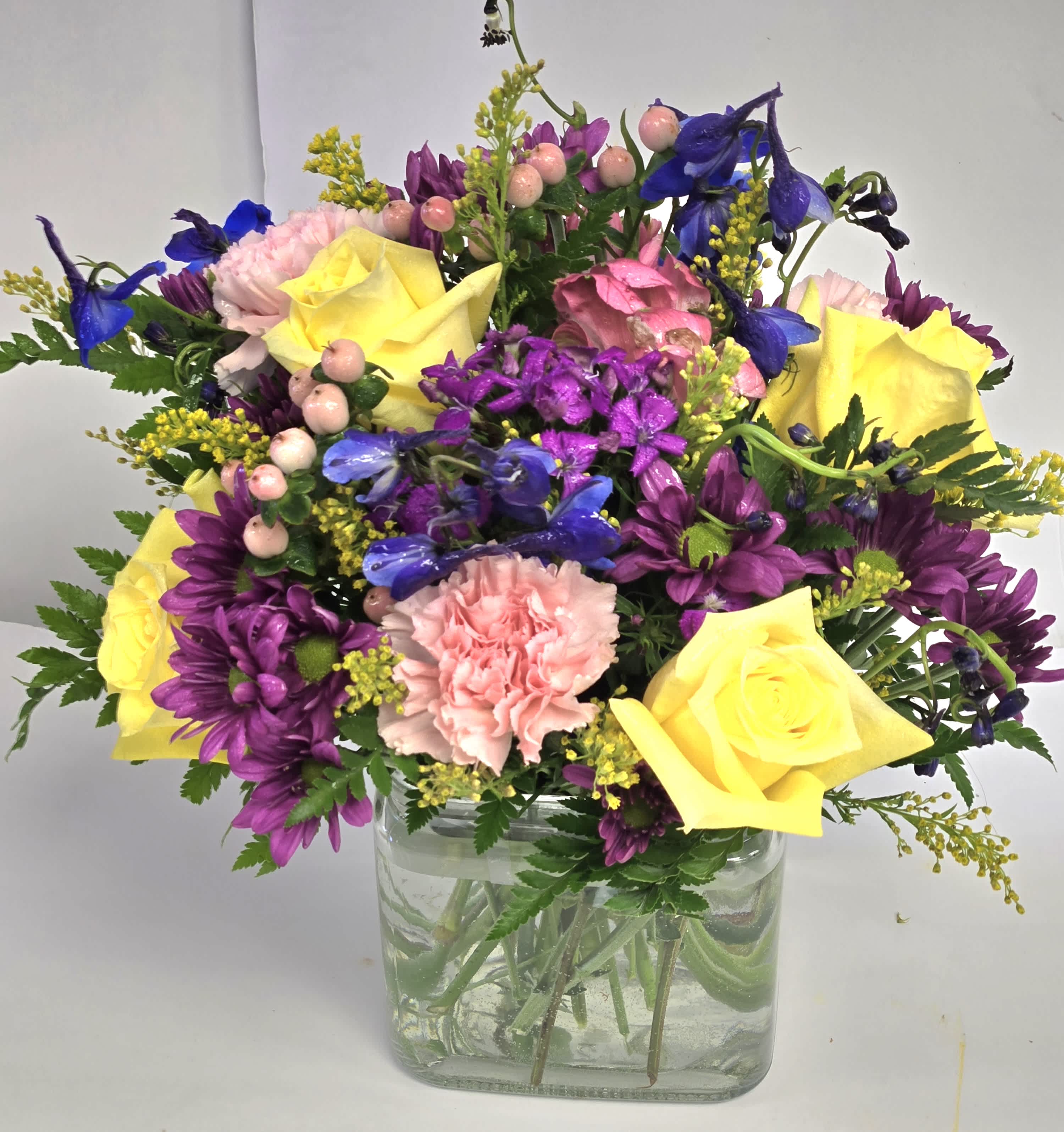 Bouquet of yellow roses, purple daisies, and pink carnations in a glass vase