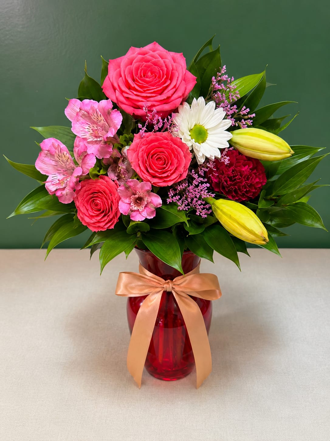 Pink roses and lilies arranged in a red vase with a ribbon