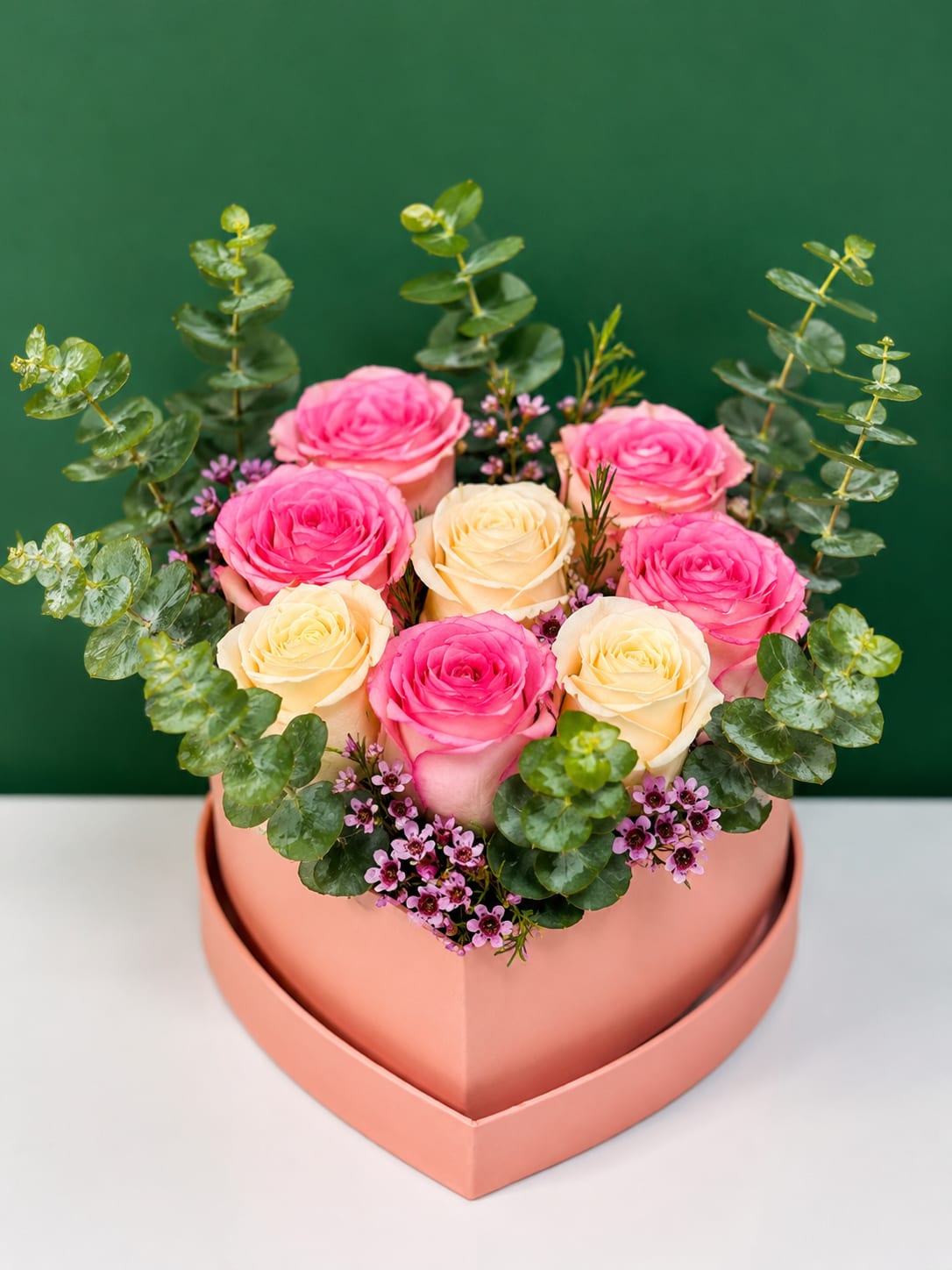 Pink and cream roses arranged in a heart-shaped box