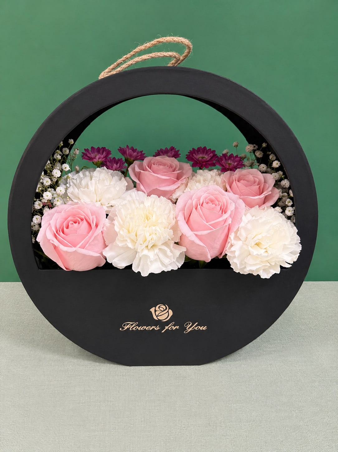 Pink roses and white carnations arranged in a round black gift box
