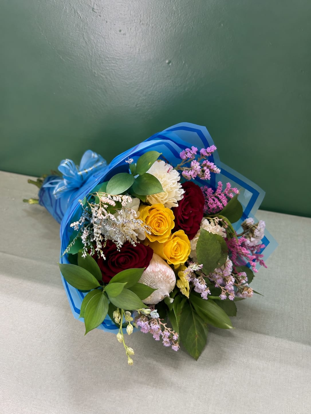 Bouquet of red, yellow, and white roses wrapped in blue paper