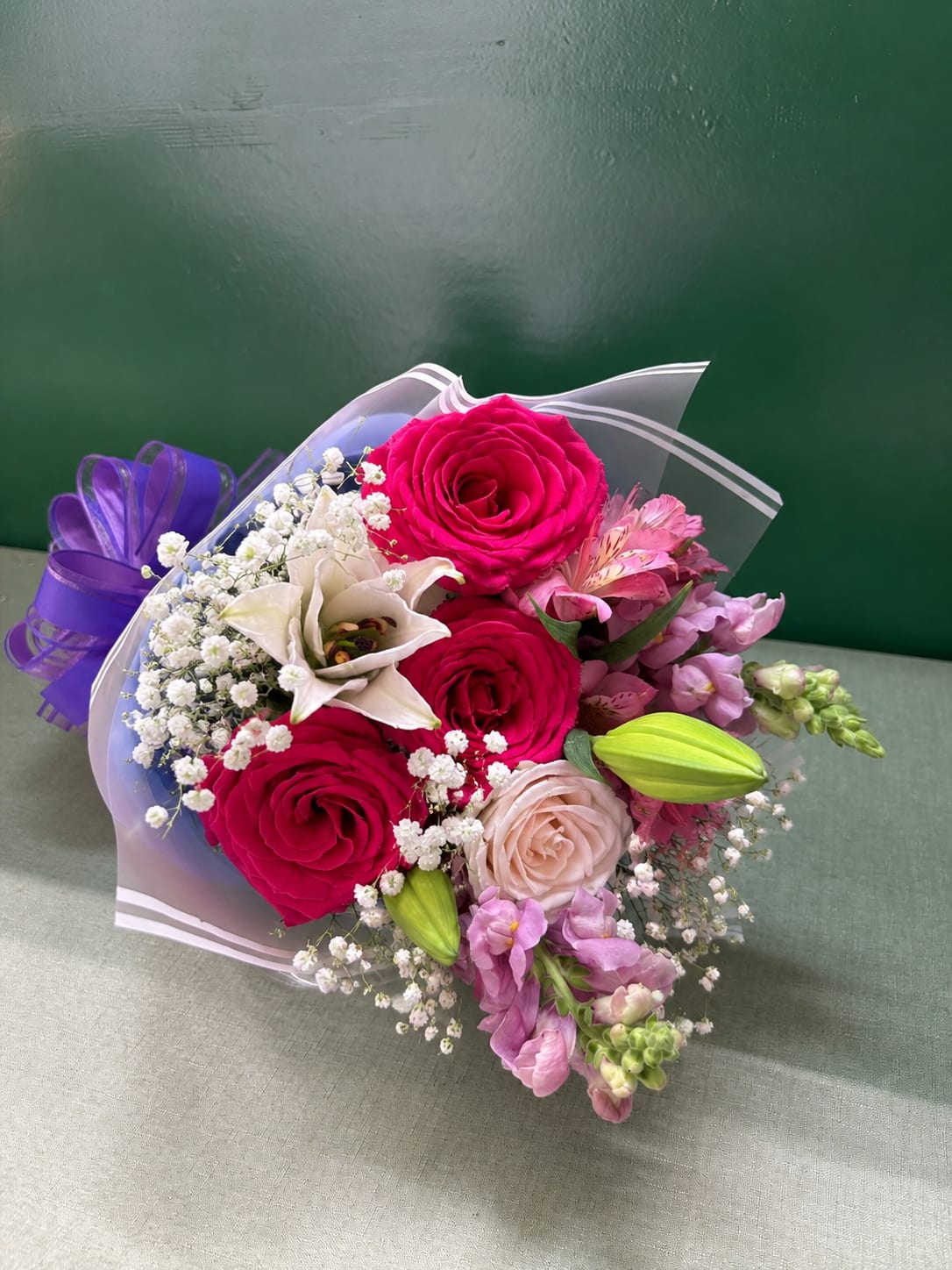 Bouquet of pink roses, white lily, and purple flowers wrapped in clear paper