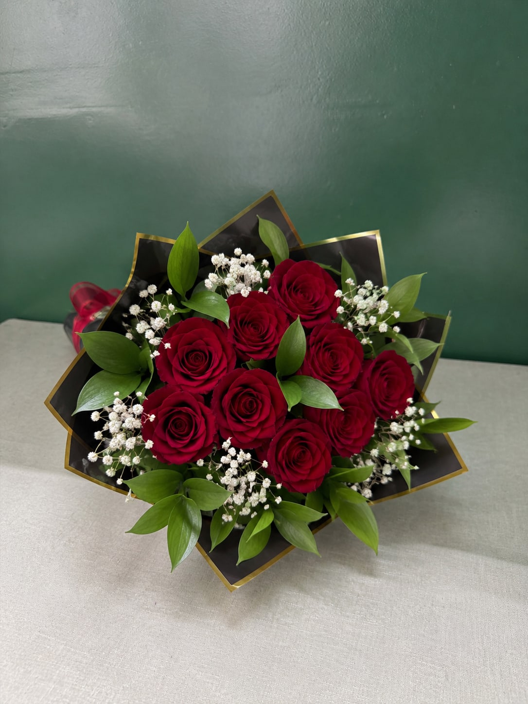 Bouquet of red roses with white baby's breath and green leaves wrapped in black paper