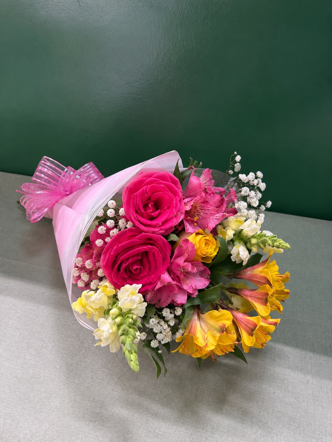 Bouquet of pink roses, pink alstroemeria, and yellow flowers wrapped in pink paper